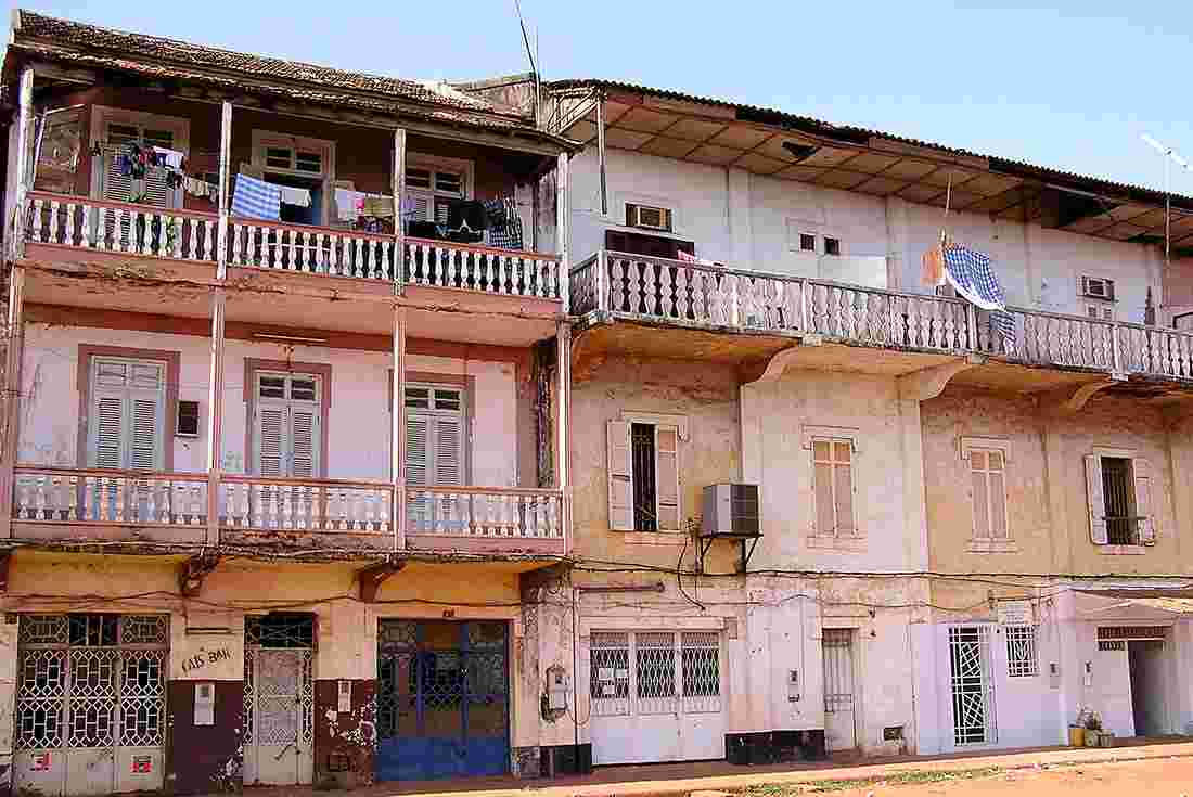 Guinea Bissau 桌布 壁紙 — 風化的殖民風格建築，帶有陽台和晾曬的衣物，在清澈的藍天下。
