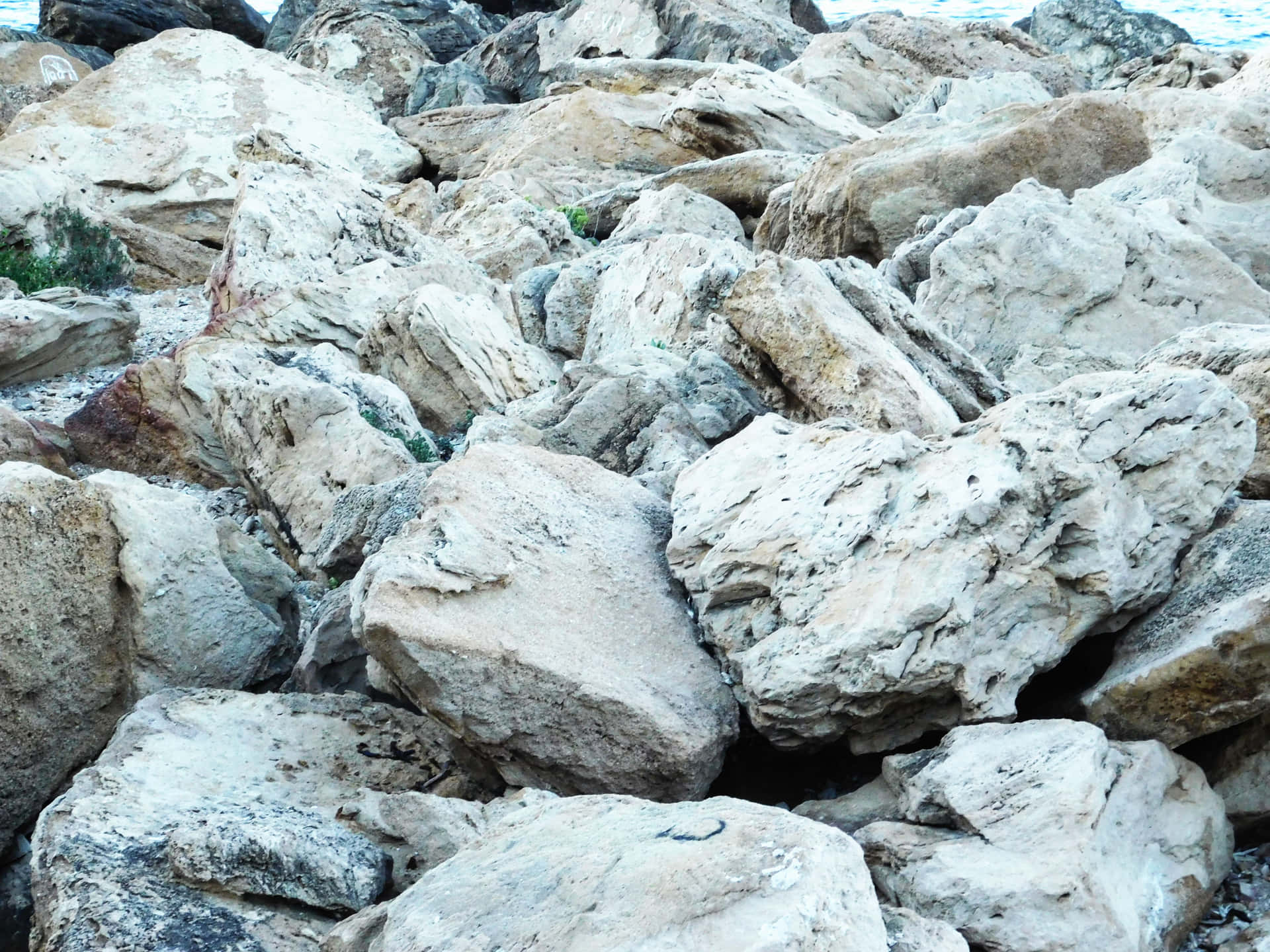 Stone texture 壁紙 — 風化的灰色和米色巨石堆疊在一起，稀疏的綠色灌木依附在裂縫中的特寫。