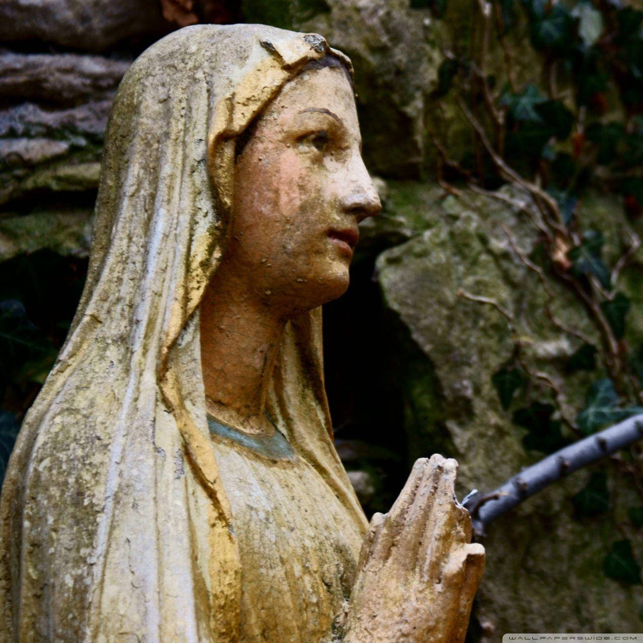 Virgin Mary 桌布 壁紙 — 風化的石像，一個戴著披紗祈禱的女人，放在長滿苔蘚的岩石和常春藤之間。