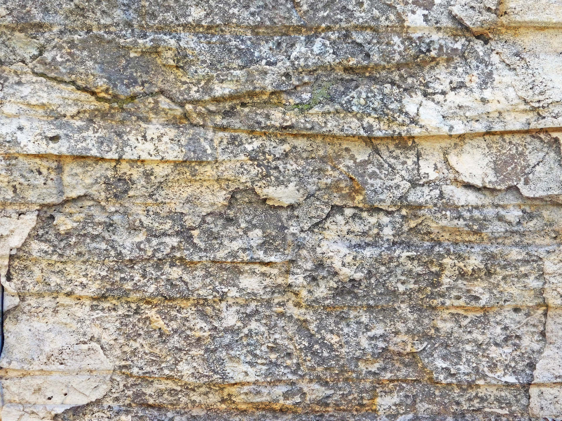Stone texture 壁紙 — 風化石牆的特寫，帶有層狀水平裂縫和地衣斑塊，呈現柔和的灰色和黃色。