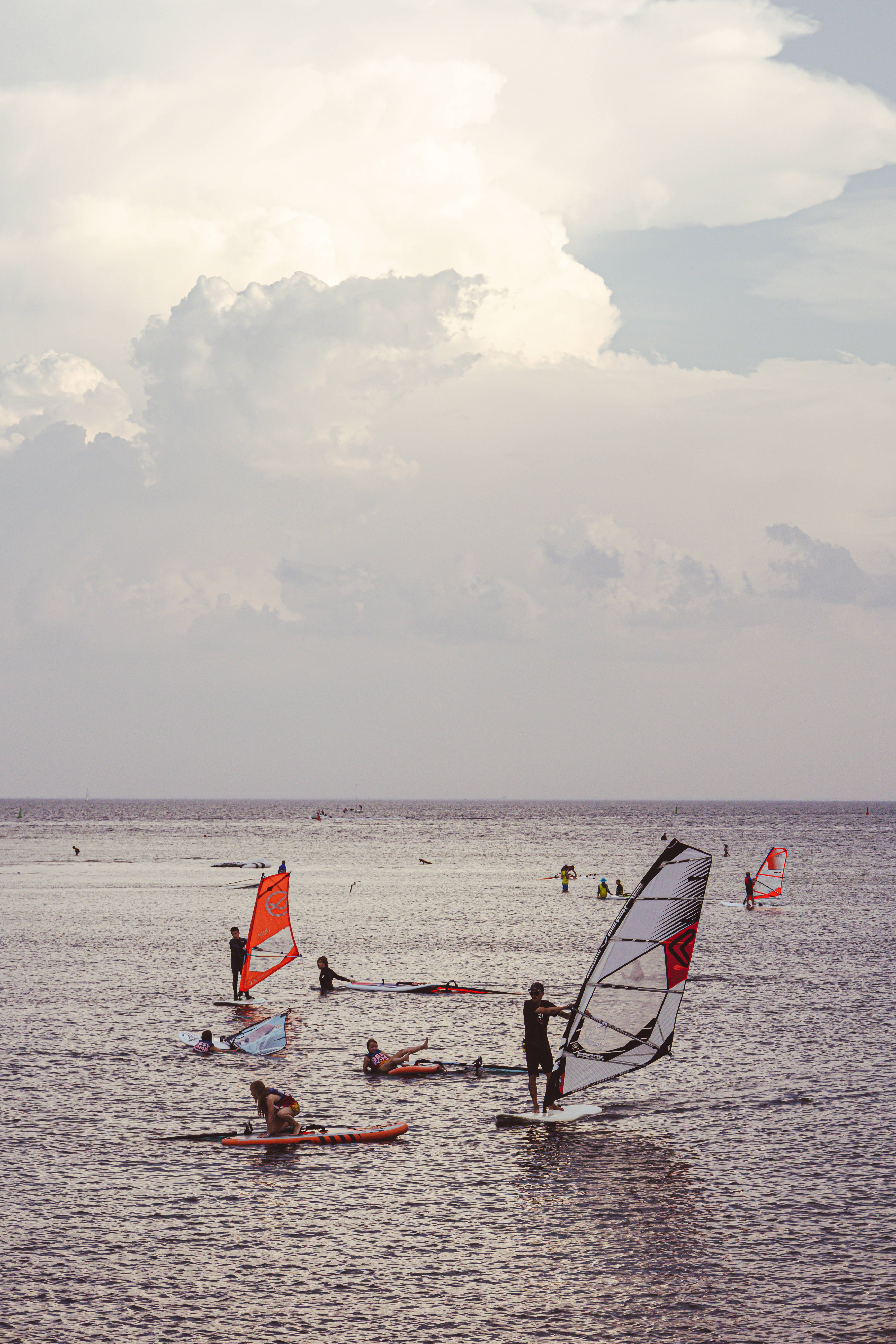 Windsurfing 桌布 壁紙 — 風帆衝浪者和槳板衝浪者在廣闊多雲的天空下，在平靜的海洋上滑行。