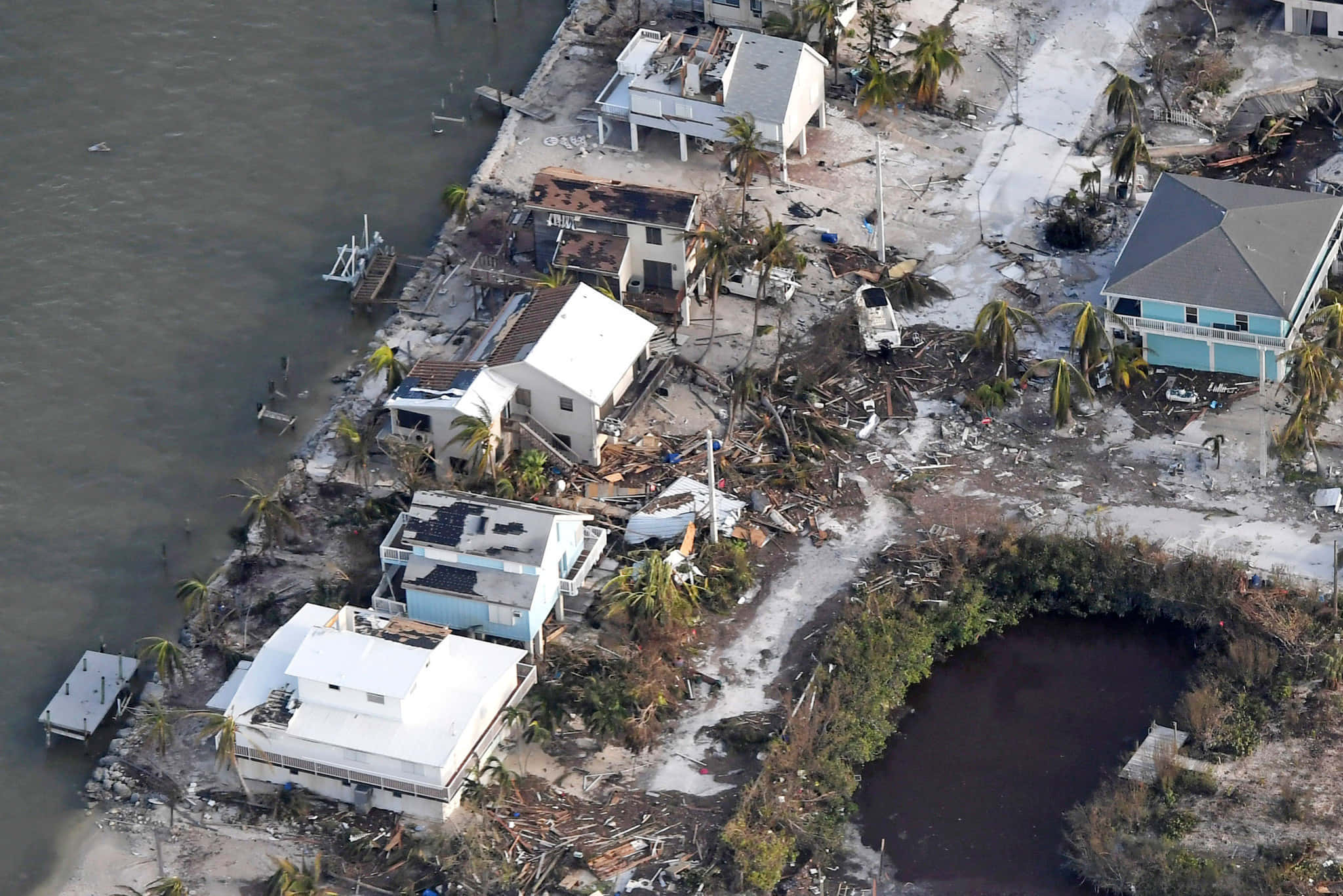 Hurricane 桌布 壁紙 — 颶風破壞的沿海房屋鳥瞰圖，屋頂破碎，碎片散落在棕櫚樹和水面上。