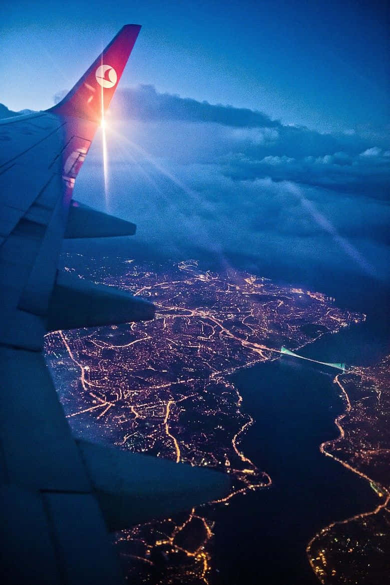 Plane 桌布 壁紙 — 飛機機翼在夕陽餘暉中閃耀，下方廣闊的城市景觀被金色燈光照亮。
