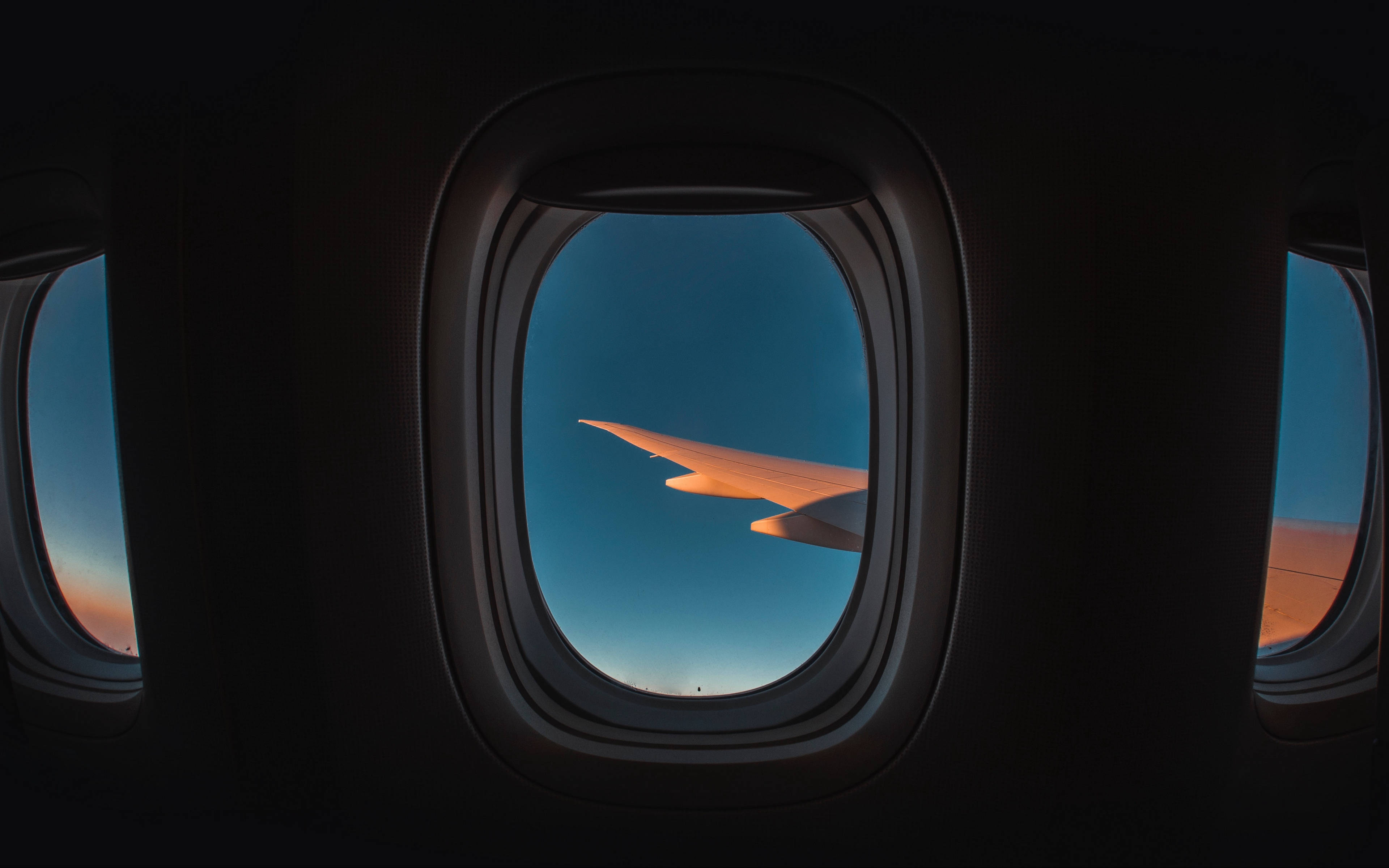 天空景色 桌布 壁紙 — 飛機機翼在暮色天空中發出琥珀色光芒，透過飛機窗戶看到黑暗的機艙內部。