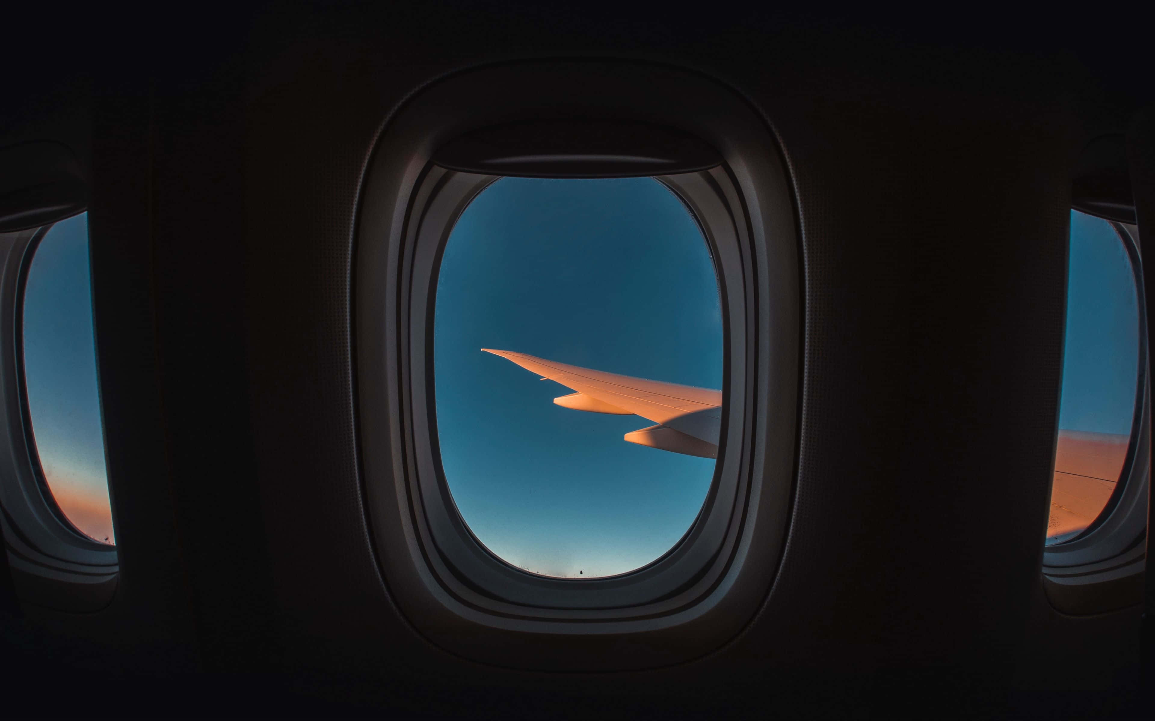 4K 飛機壁紙 桌布 壁紙 — 飛機機翼在暮色天空中透過飛機窗戶閃爍琥珀色光芒，機艙內部昏暗。