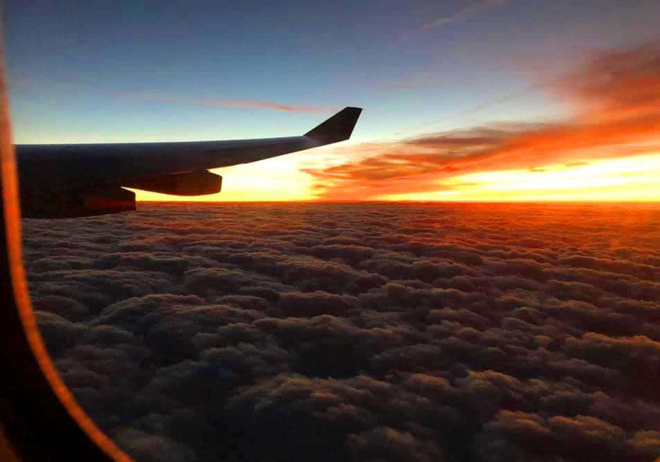 Airplane Window 桌布 壁紙 — 飛機機翼在無盡棉花糖雲層之上，以火紅夕陽為背景形成剪影。