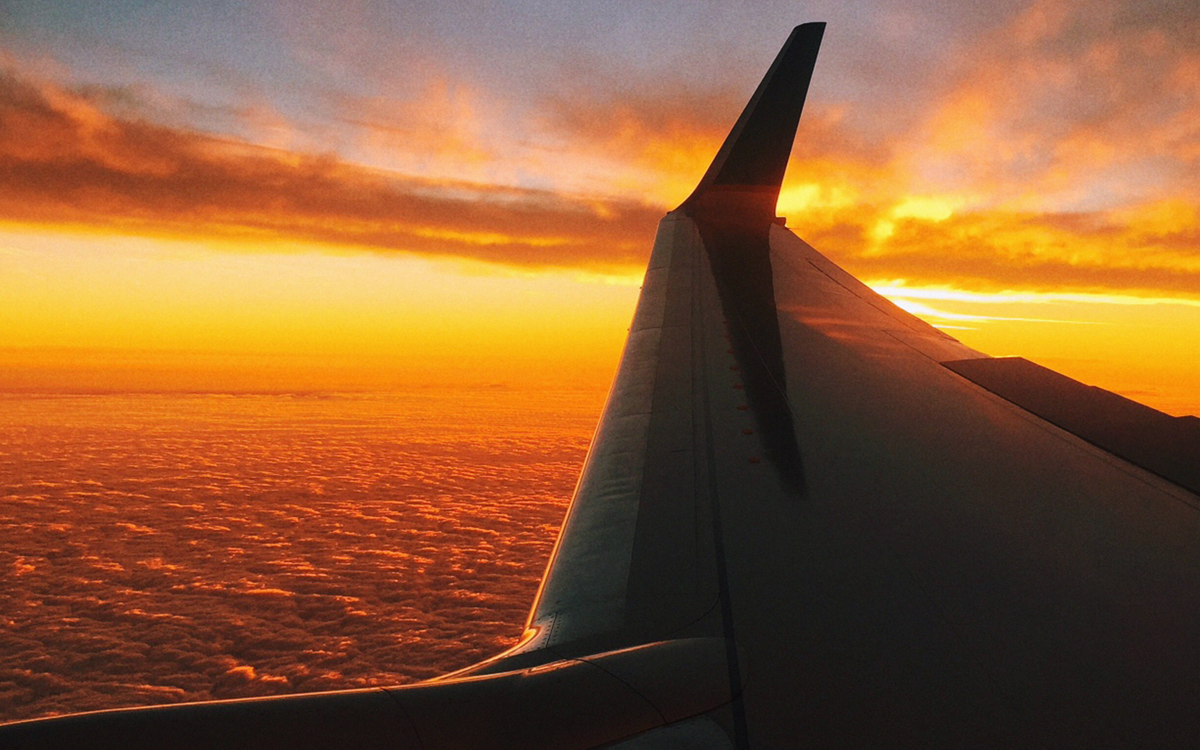 飛機 桌布 壁紙 — 飛機機翼在無盡雲海上空，以火熱橙色夕陽為背景呈現剪影。