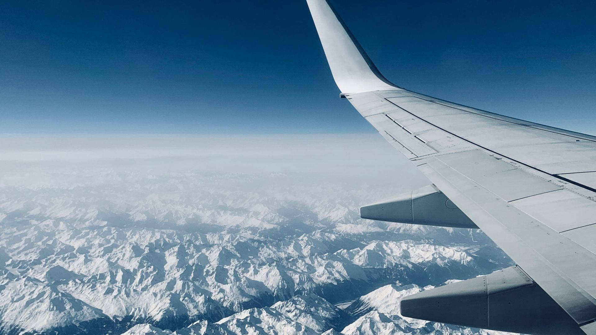View 桌布 壁紙 — 飛機機翼延伸在廣闊的雪山之上，天空清澈湛藍。