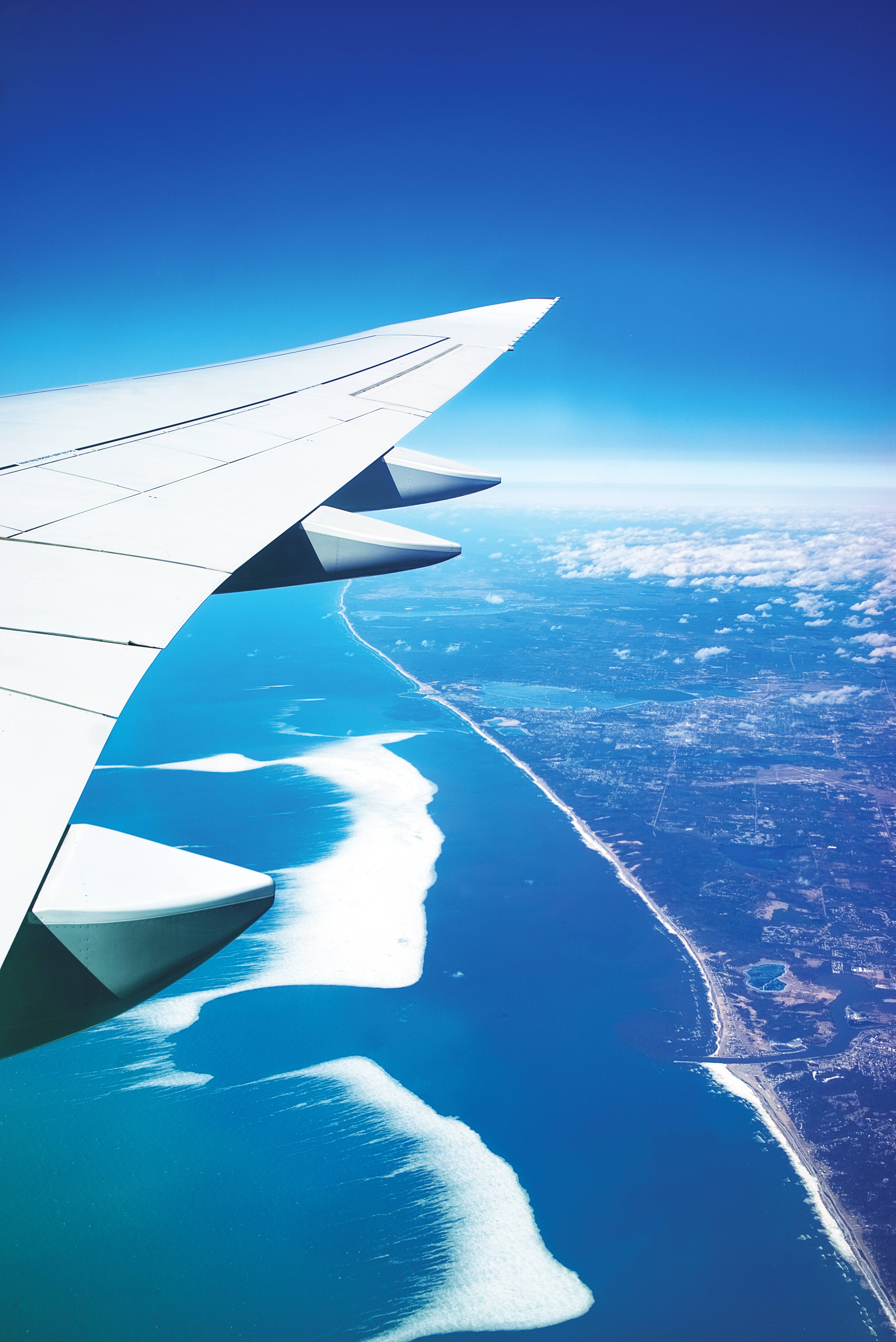 Plane 桌布 壁紙 — 飛機機翼延伸在碧綠海洋和海岸線之上，在清澈藍天下。