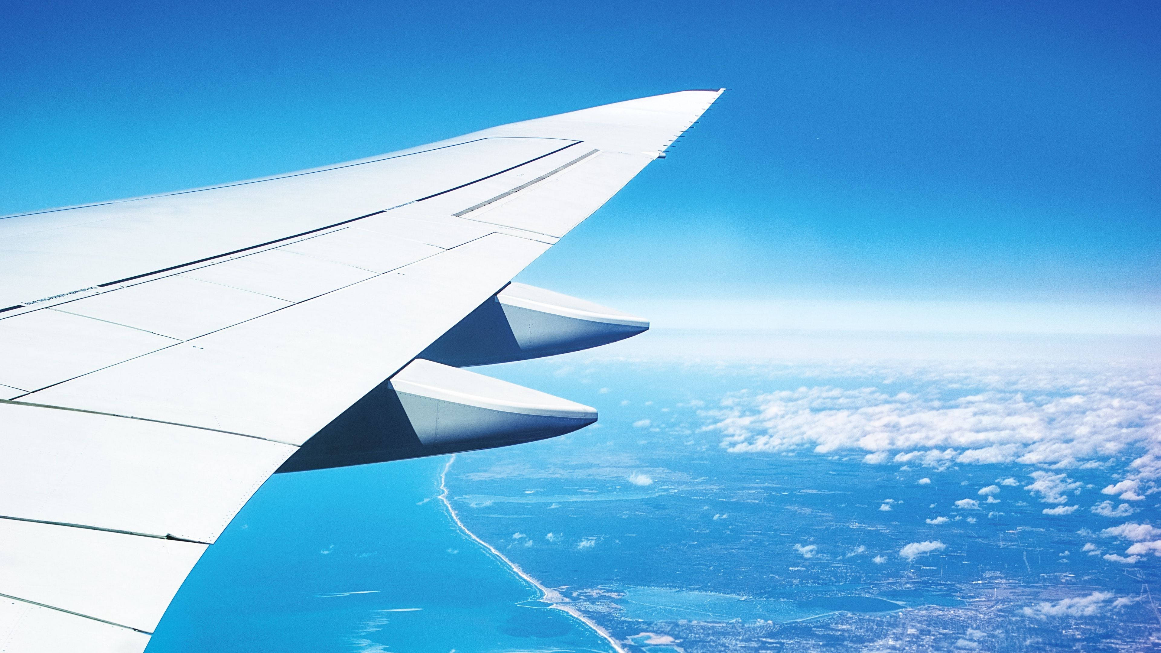 4K 飛機壁紙 桌布 壁紙 — 飛機機翼延伸在碧綠海洋和白色雲朵之上，在清澈藍天下。