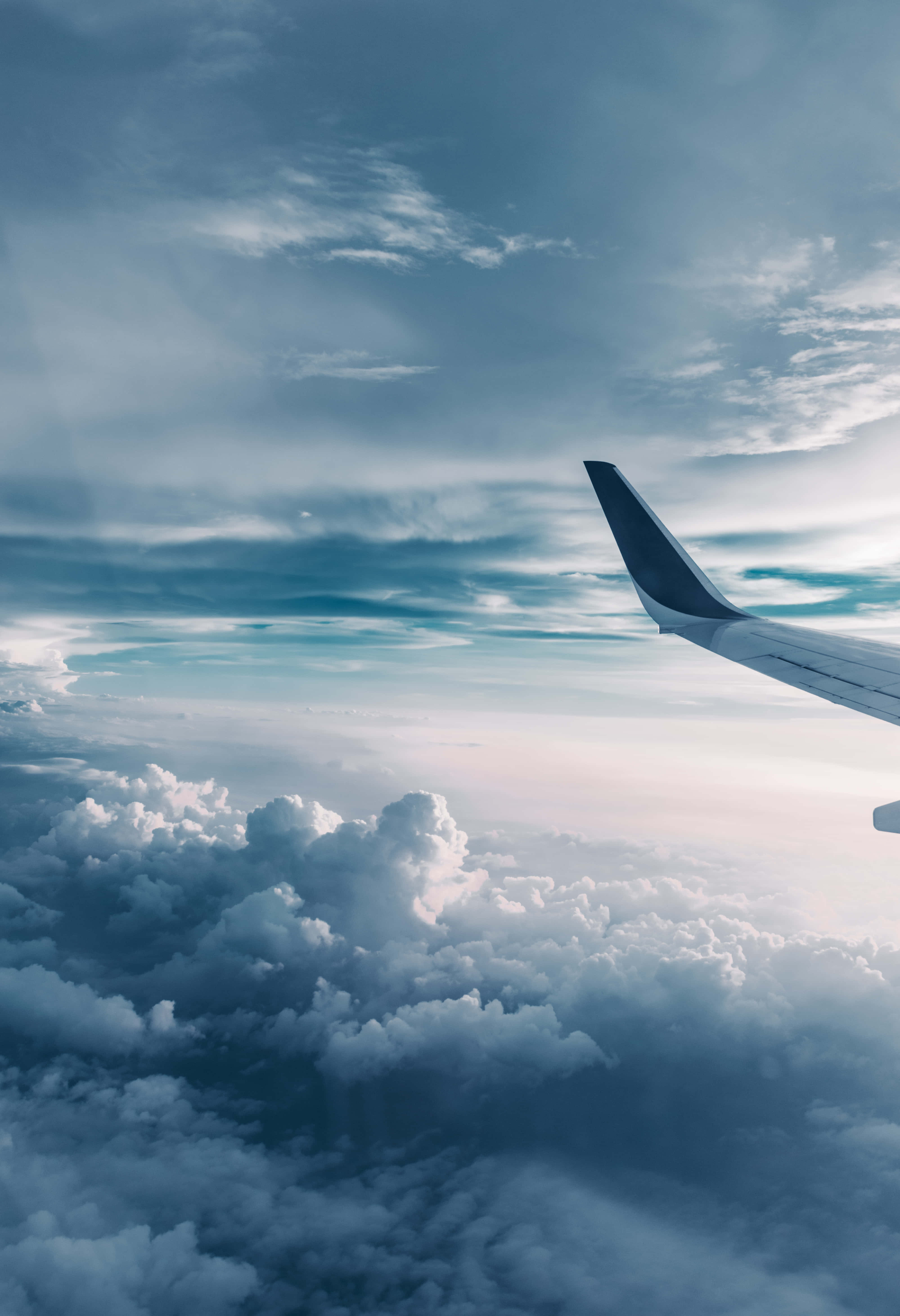 Aviation 桌布 壁紙 — 飛機機翼延伸在蓬鬆白雲的海洋之上，下方是廣闊的藍天，點綴著縷縷卷雲。