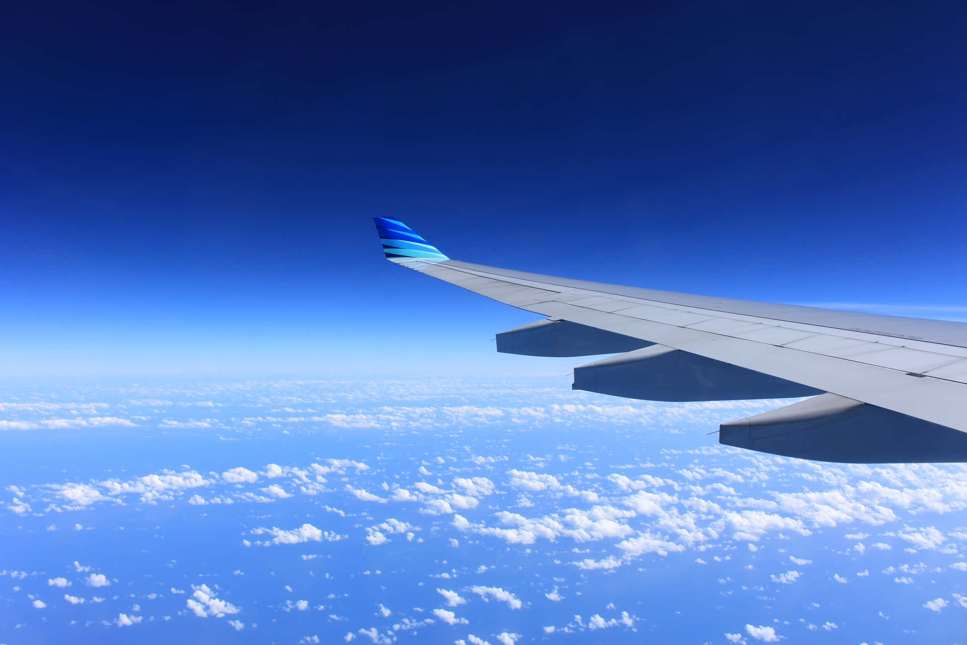 飛機 桌布 壁紙 — 飛機機翼延伸在蓬鬆的白雲之上，下方是廣闊清澈的藍天。