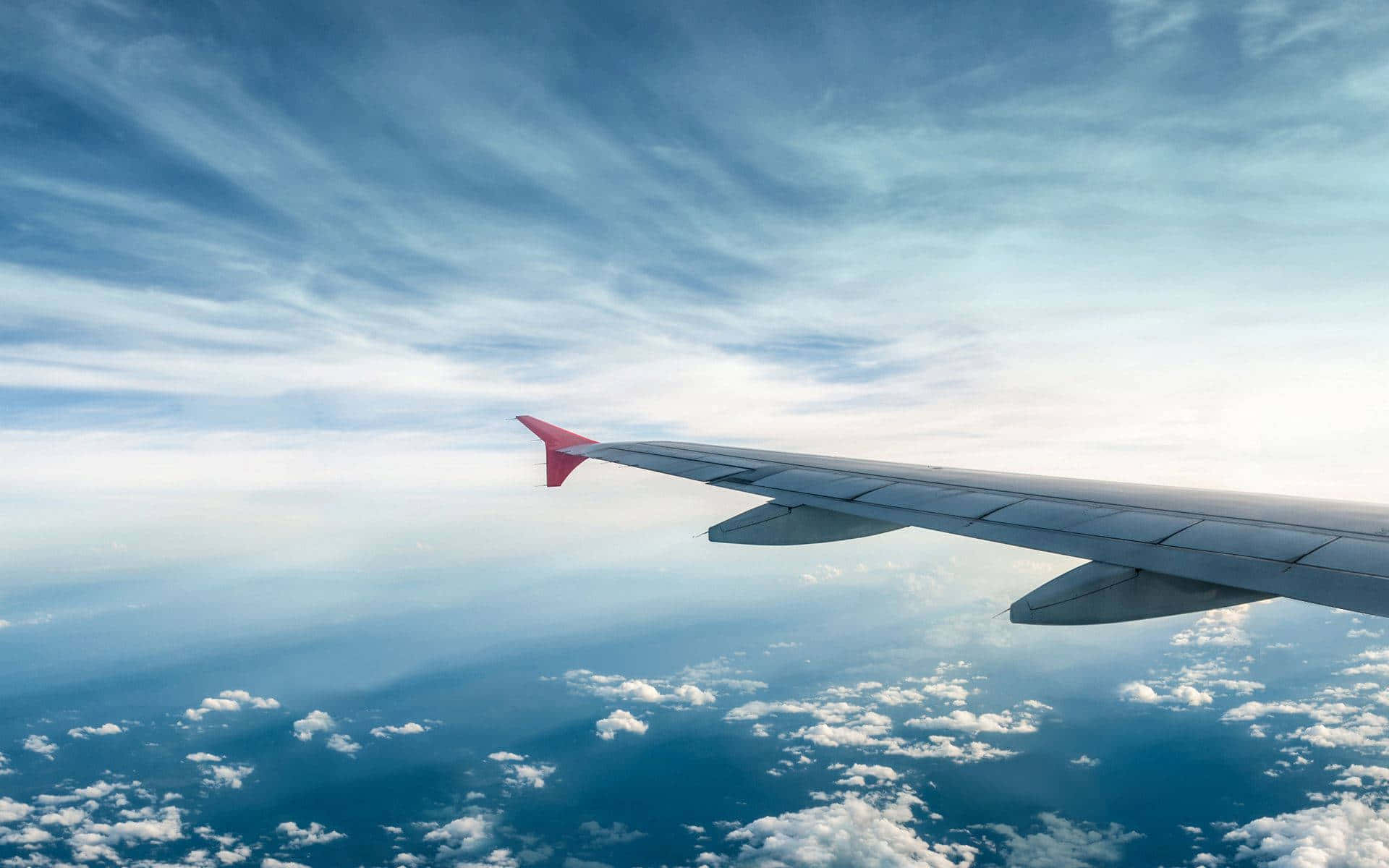 飛機 桌布 壁紙 — 飛機機翼延伸在蓬鬆的白雲之上，下方是廣闊的藍天，點綴著縷縷卷雲。