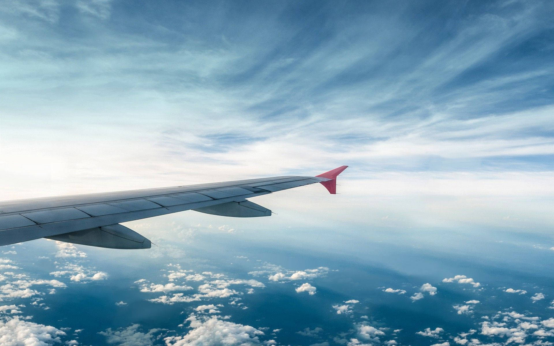 4K 飛機壁紙 桌布 壁紙 — 飛機機翼延伸至蓬鬆的白雲之上，下方是廣闊的藍天，點綴著縷縷卷雲。