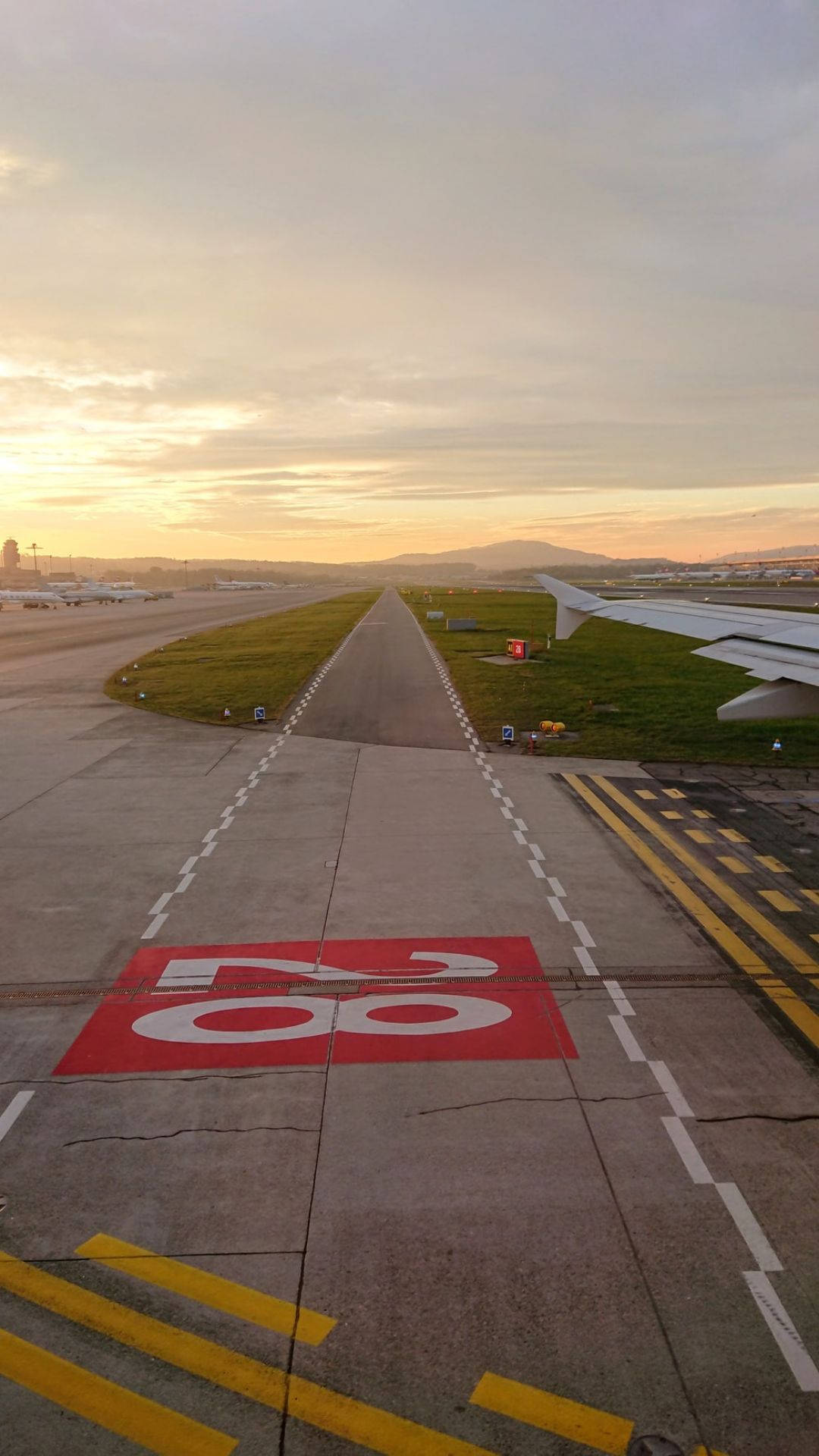 Runway 桌布 壁紙 — 飛機翼俯瞰跑道68在黎明時分，柔和的金色光芒和遠山在粉彩天空下。