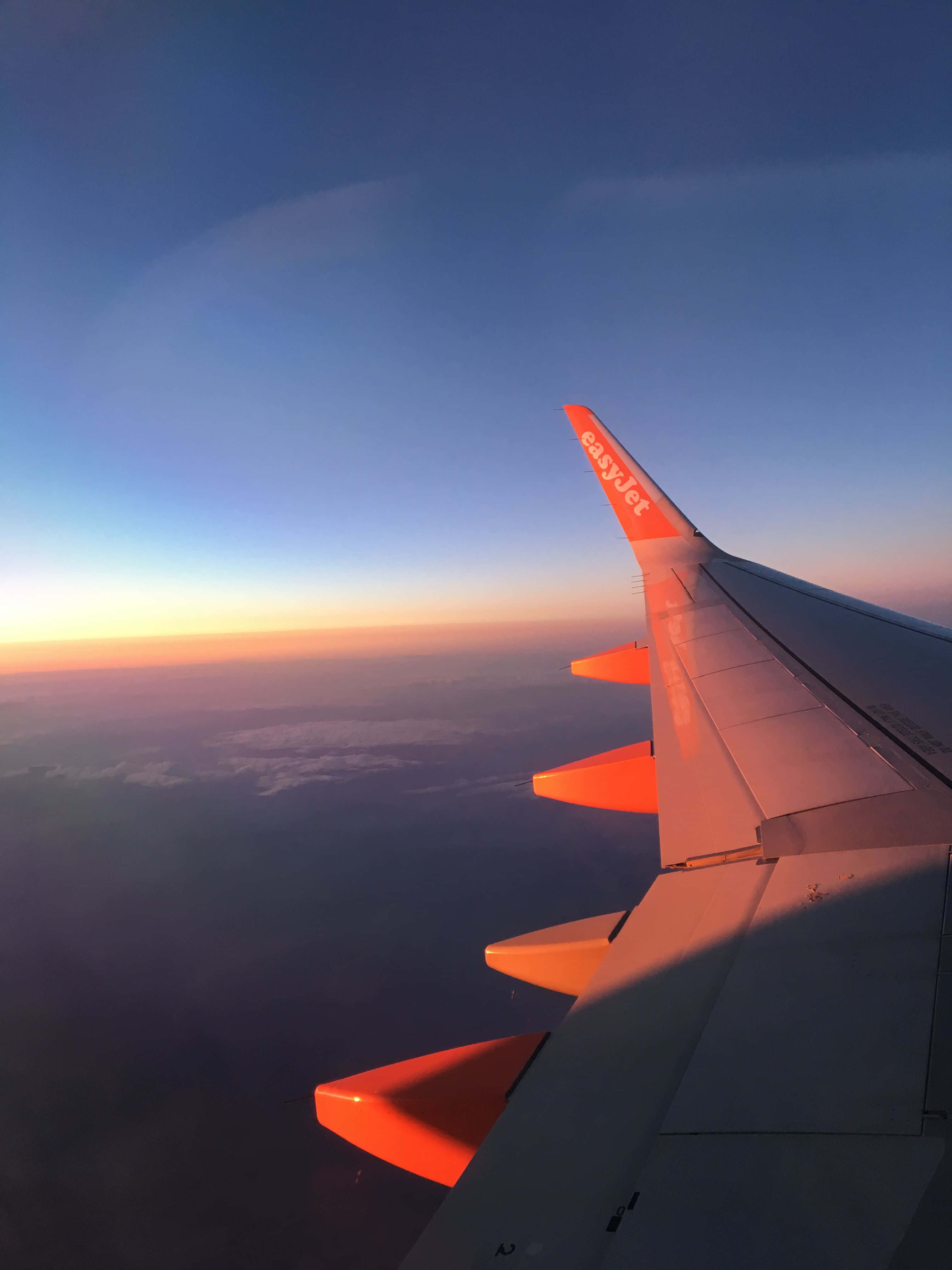 Plane 桌布 壁紙 — 飛機翼帶橙色尖端在日落光線中發光，映襯著雲層之上的漸變天空。