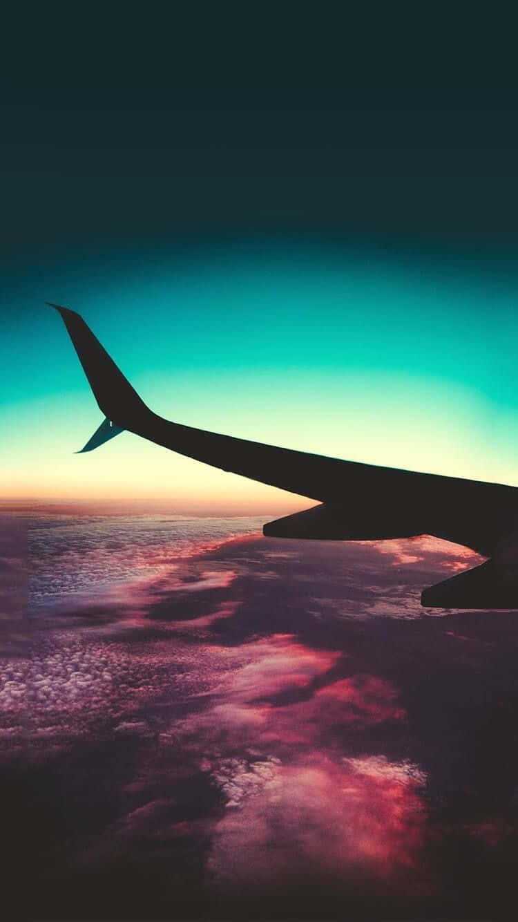 Plane 桌布 壁紙 — 飛機翼的剪影，背景是充滿活力的日落天空，下方有粉紅色、紫色和藍綠色的雲。