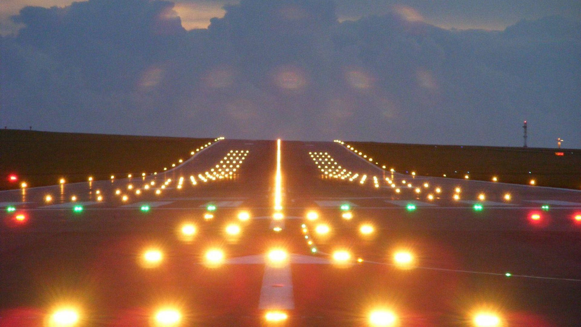 Runway 桌布 壁紙 — 飛機跑道燈在陰雲密布的黃昏地平線下延伸至暮色天空。