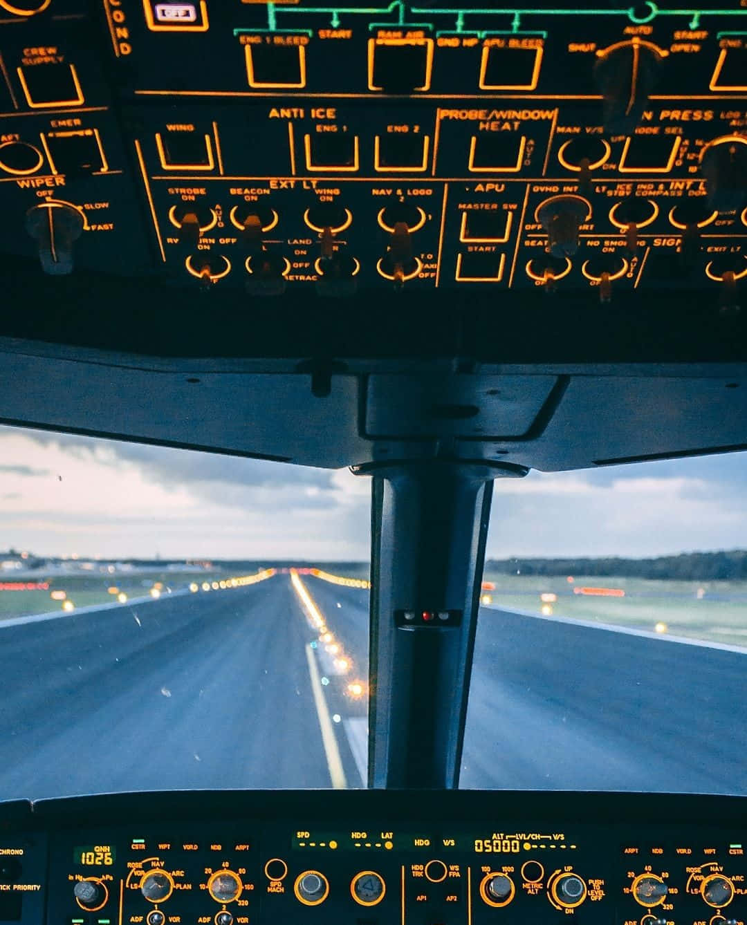 Plane 桌布 壁紙 — 飛機駕駛艙儀表板發出琥珀色光芒，飛機在黃昏時滑行跑道，前方城市燈光閃爍。