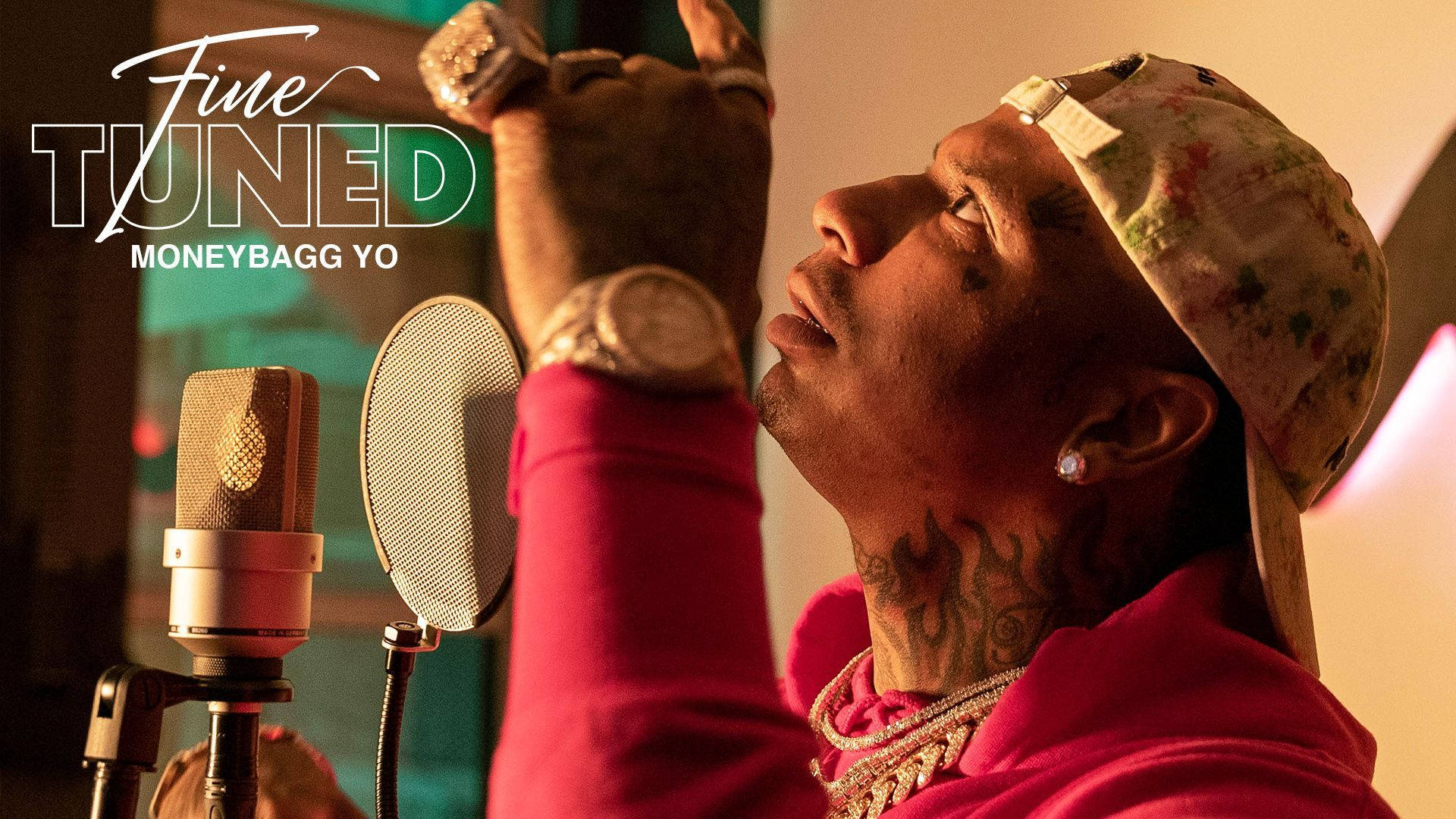 Yo 桌布 壁紙 — 饒舌歌手 Moneybagg Yo 身穿粉紅色連帽衫和花卉圖案帽子，在溫暖照明的錄音室中錄音時向上做手勢。