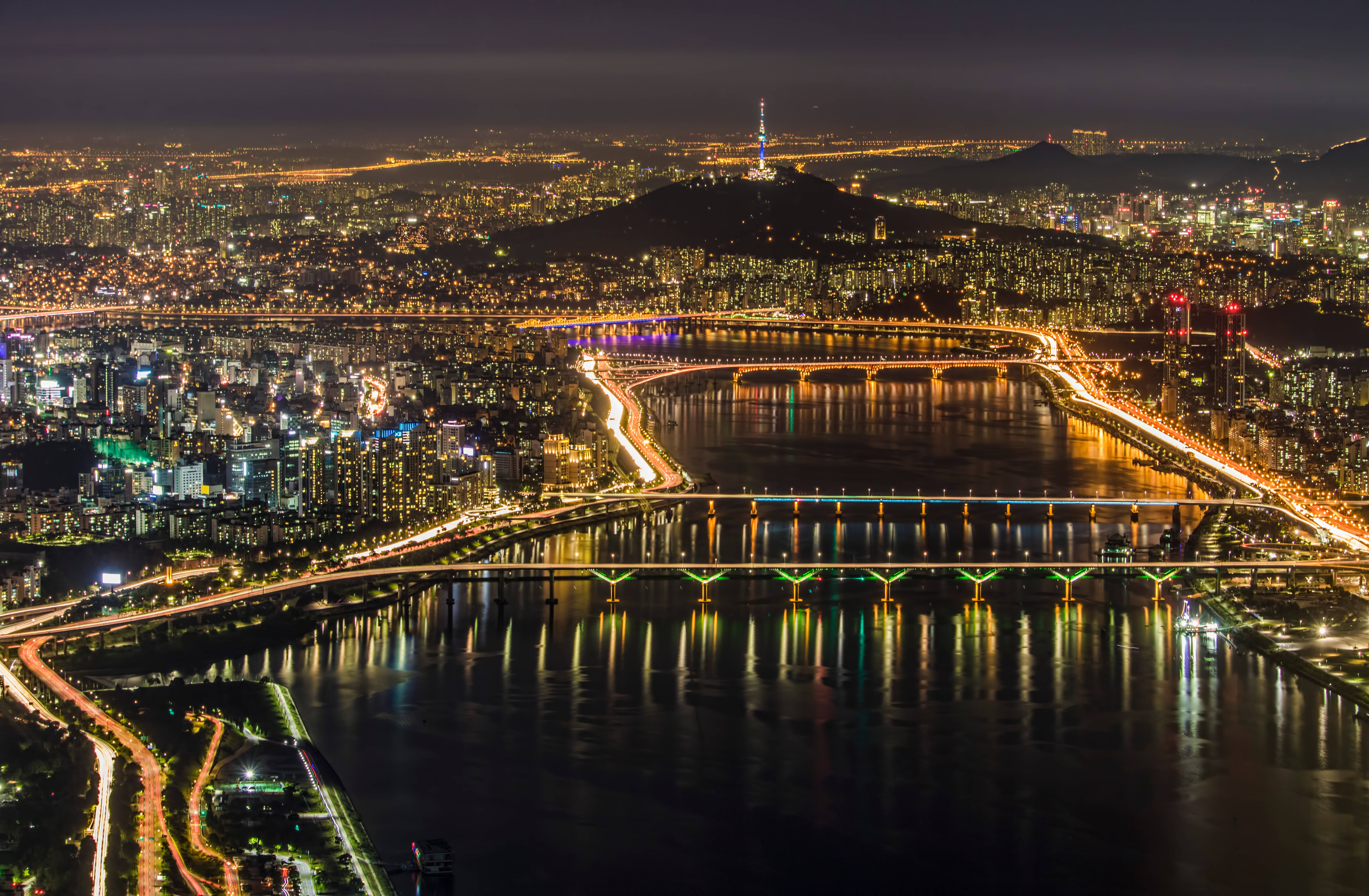 南韓 桌布 壁紙 — 首爾夜間空中景觀，燈火輝煌的城市天際線，發光的橋樑橫跨黑暗的河流，N首爾塔矗立在山丘上。