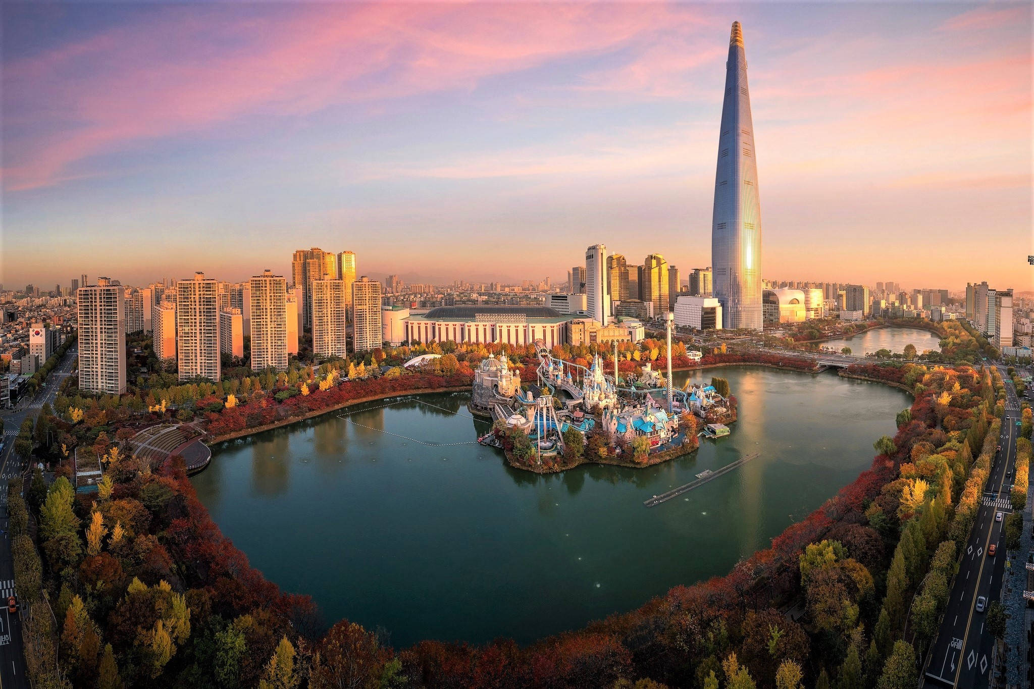 South Korea 桌布 壁紙 — 首爾日落時的鳥瞰圖，樂天世界塔和圍繞著湖泊的秋樹，湖泊旁有一個遊樂園。