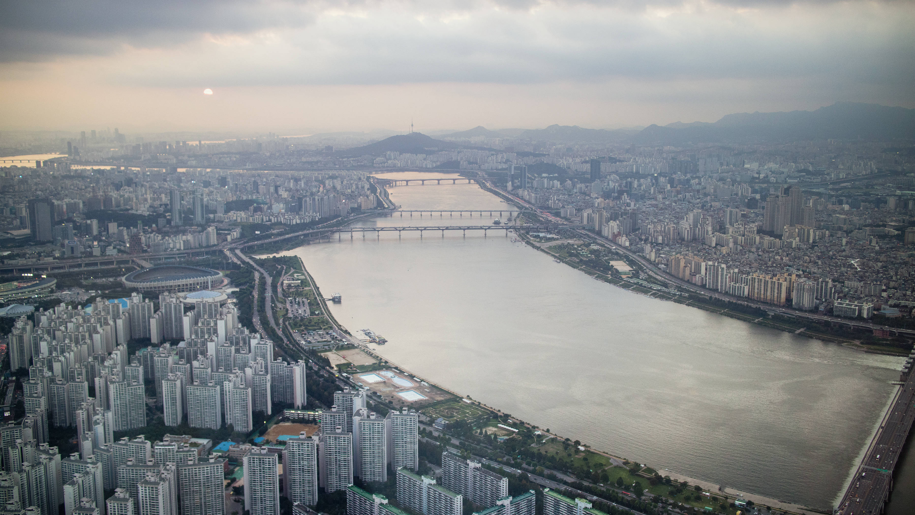 首爾 桌布 壁紙 — 首爾沿漢江的城市擴張的鳥瞰圖，在朦朧的暮色天空下，遠山可見。