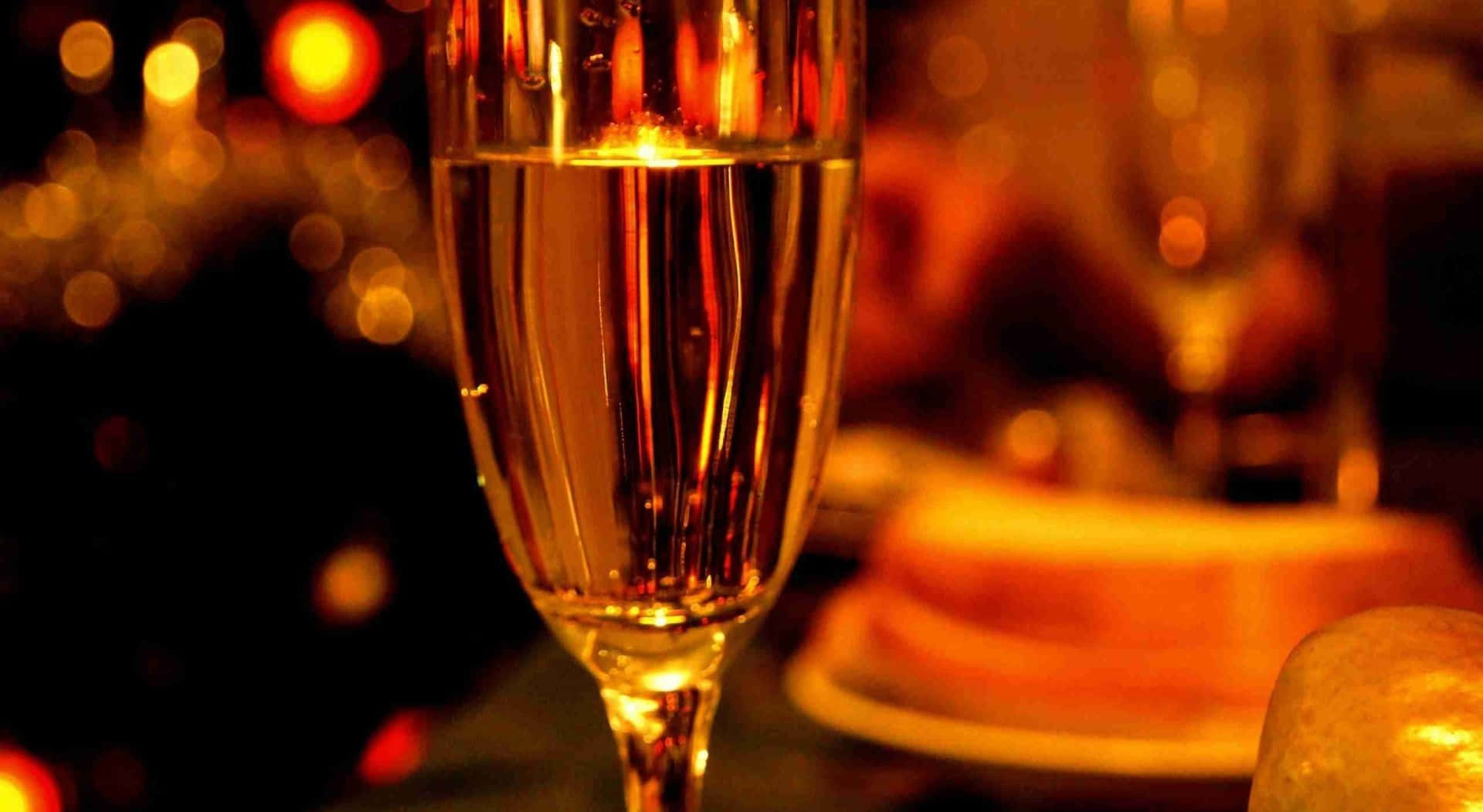 White Wine 桌布 壁紙 — 香檳杯的特寫，在模糊的暖色散景背景下閃耀著金色光芒。