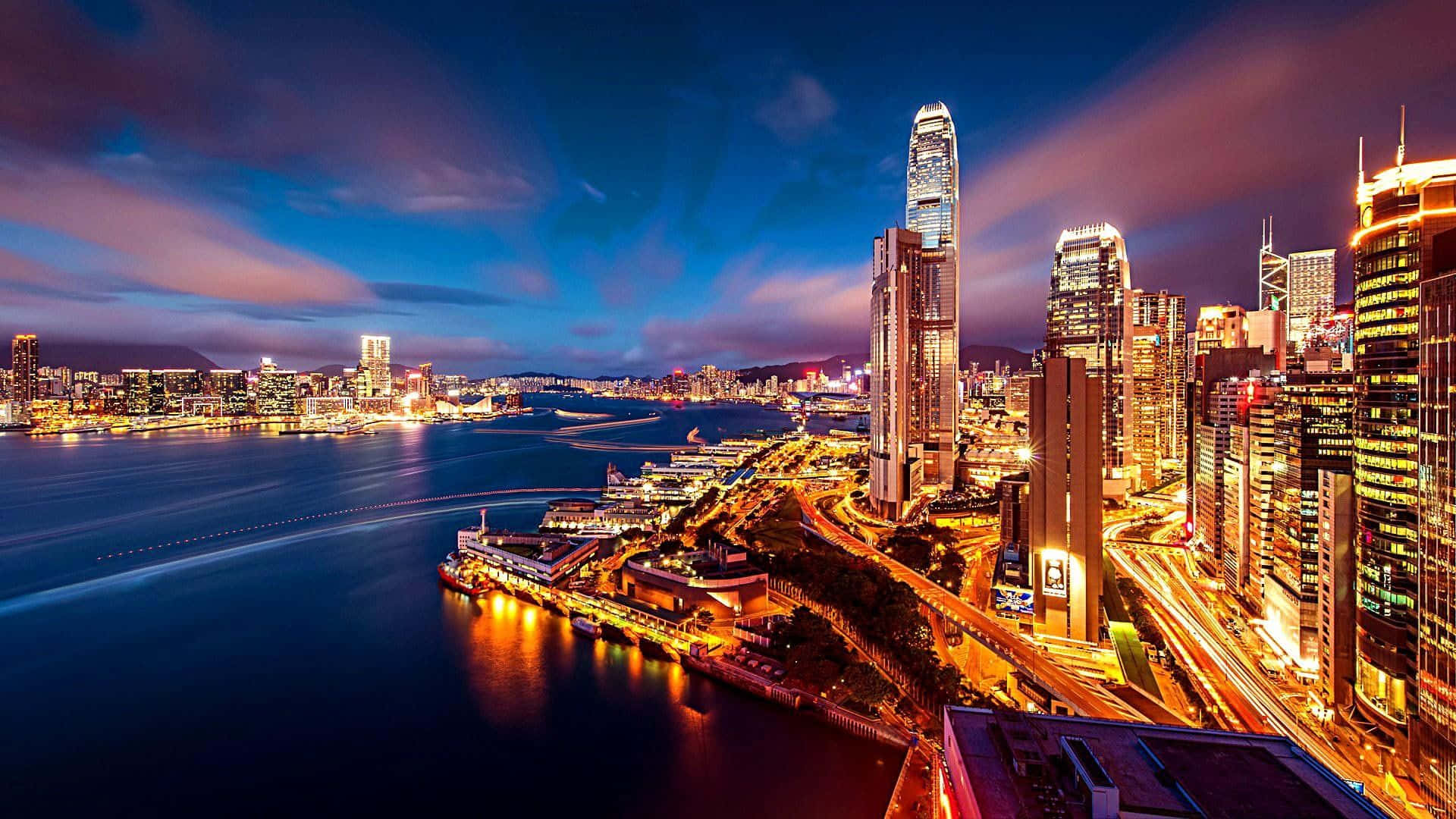 City Lights 桌布 壁紙 — 香港令人目眩的夜景，摩天大樓在深藍色天空下的海港中閃爍倒映。