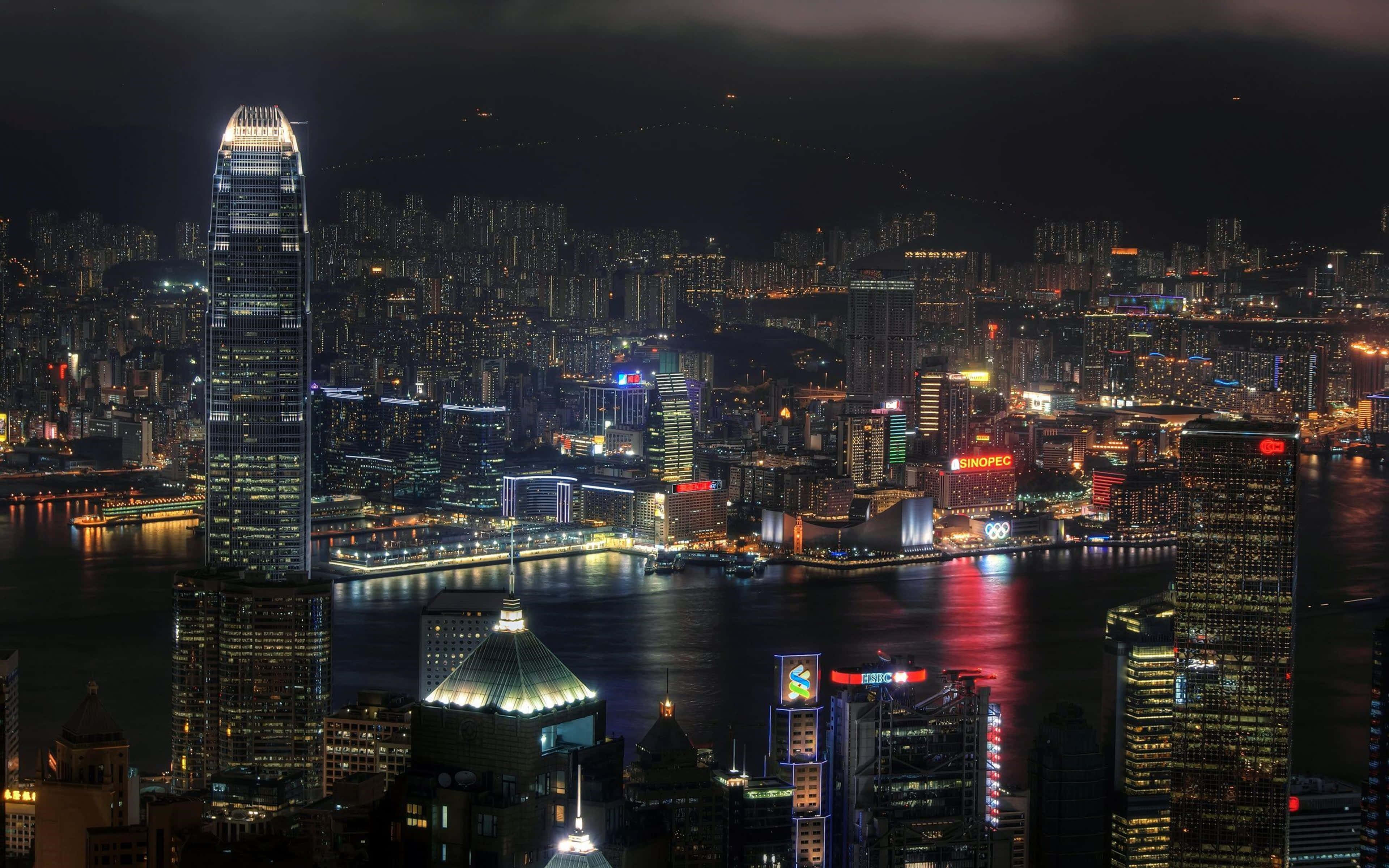 彩色動圖 桌布 壁紙 — 香港令人目眩的夜景，高聳的摩天大樓在漆黑的天空下閃耀，並倒映在水面上。