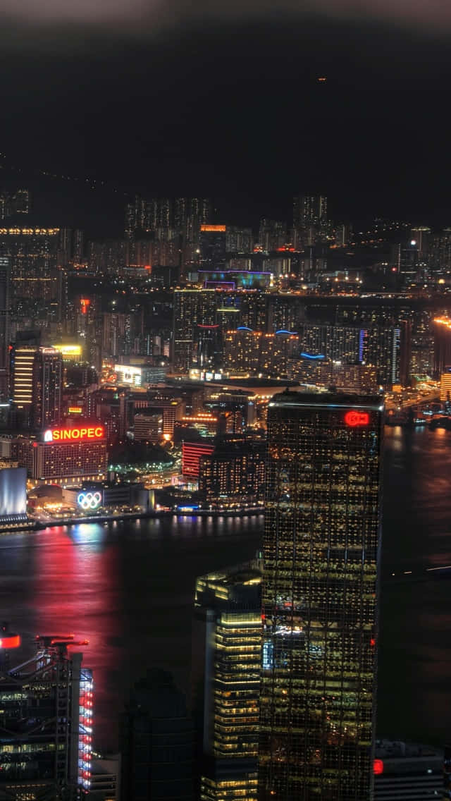 iPhone 5s 桌布 壁紙 — 香港令人目眩神迷的夜景，高聳的摩天大樓在黑暗的天空中閃耀， vibrant 燈光在水面上反射。