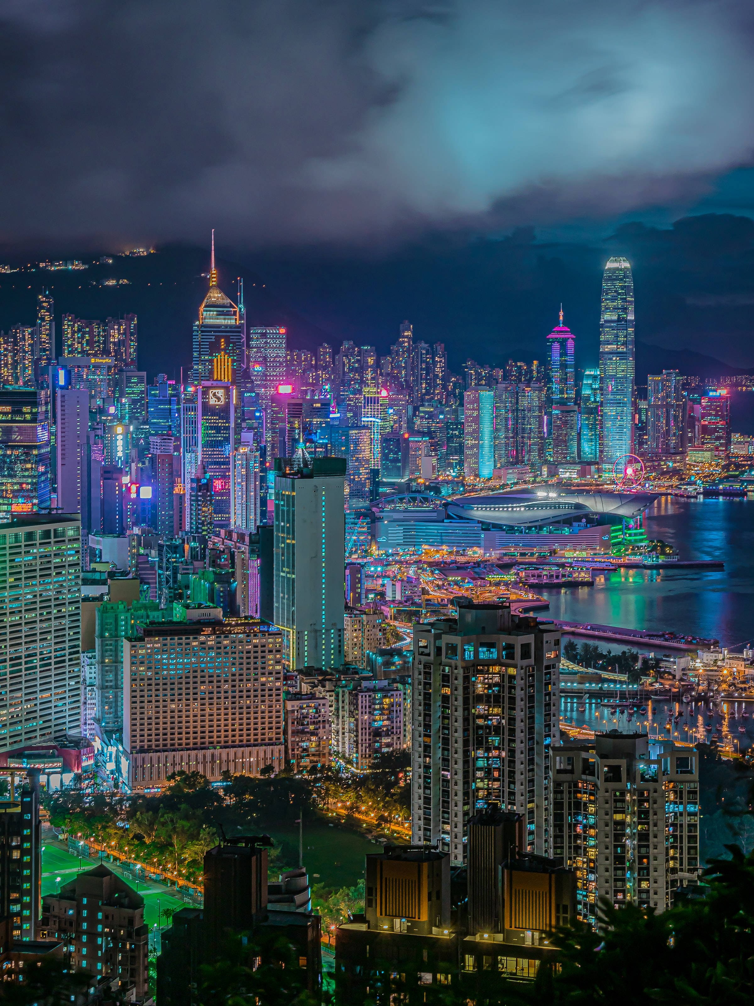 夜空 桌布 壁紙 — 香港令人驚嘆的夜景，霓虹燈閃爍的摩天大樓在陰沉天空下倒映在海港中。