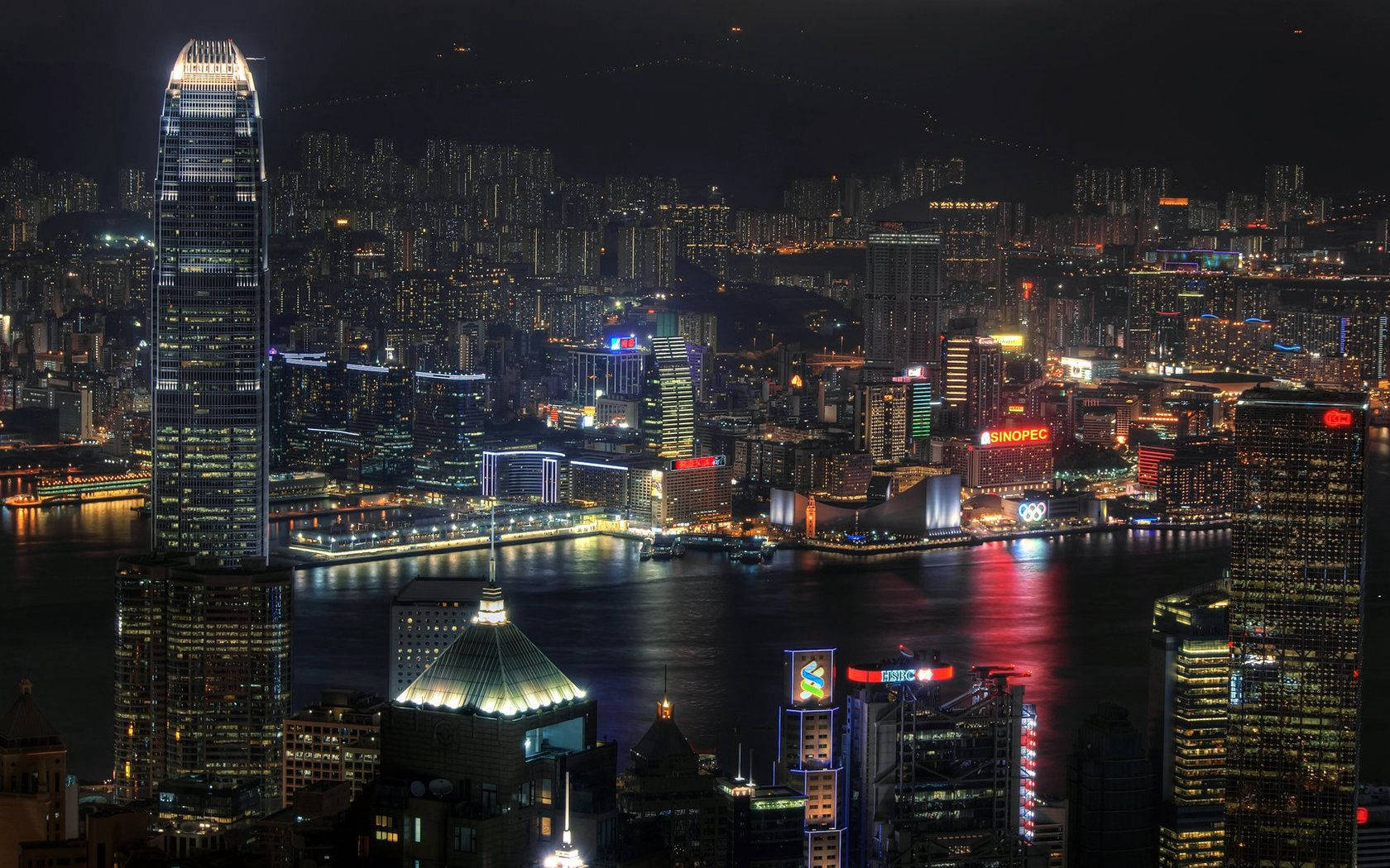 霓虹城市動態圖 桌布 壁紙 — 香港令人驚嘆的夜景，高聳的摩天大樓在黑暗的天空中閃耀， vibrant 的燈光在水面上反射。