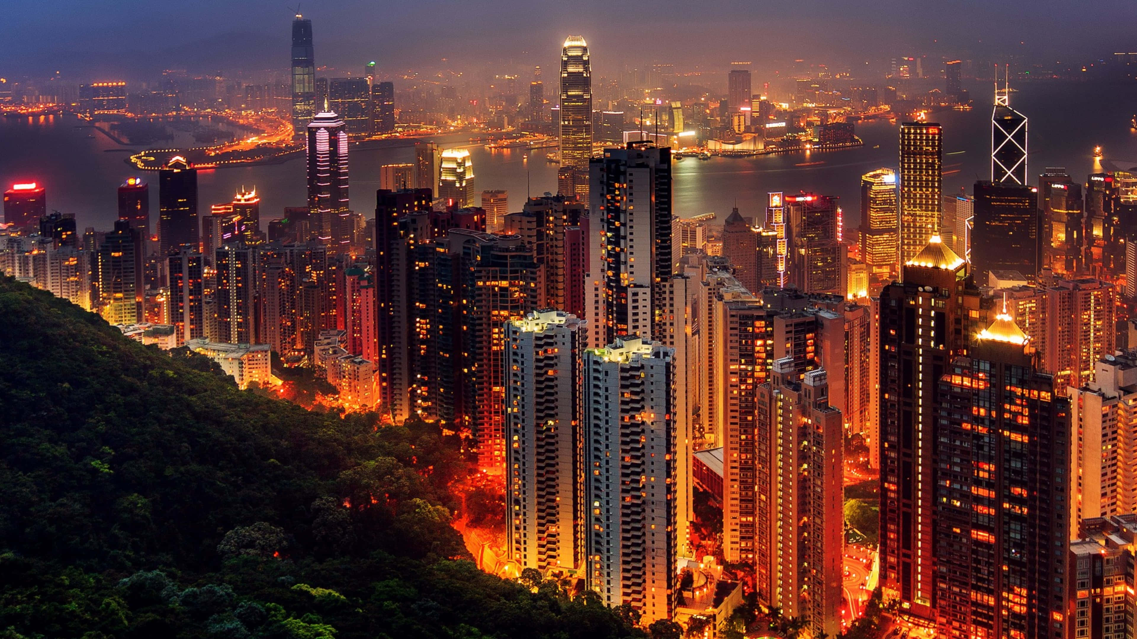UHD 桌布 壁紙 — 香港在黃昏時的空中景觀，密集的摩天大樓和港口反射著溫暖的城市燈光，天際線閃爍發光。