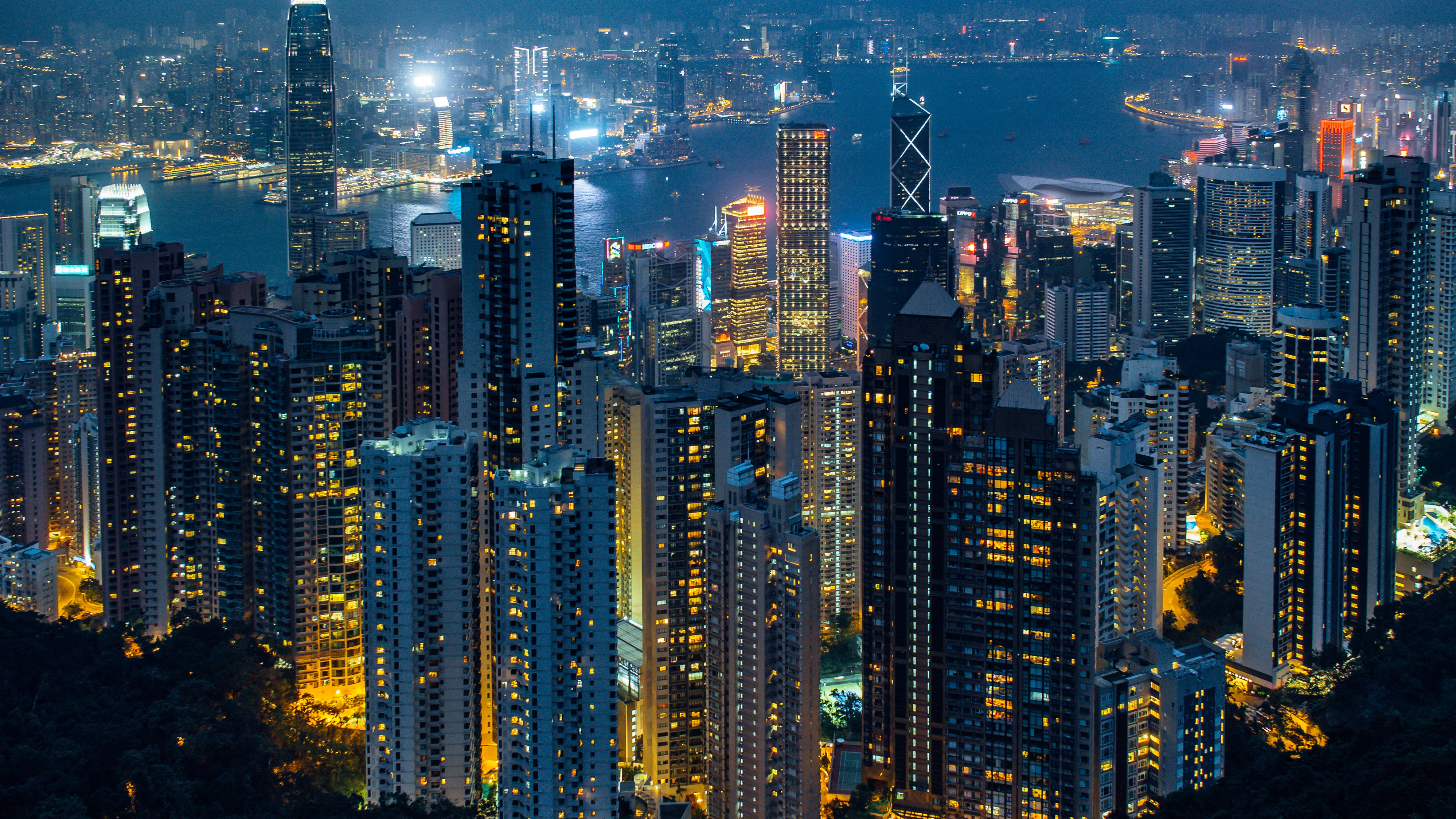 桌布 壁紙 — 香港夜晚璀璨天際線的鳥瞰圖，閃爍的摩天大樓和港口燈光倒映在水面上。