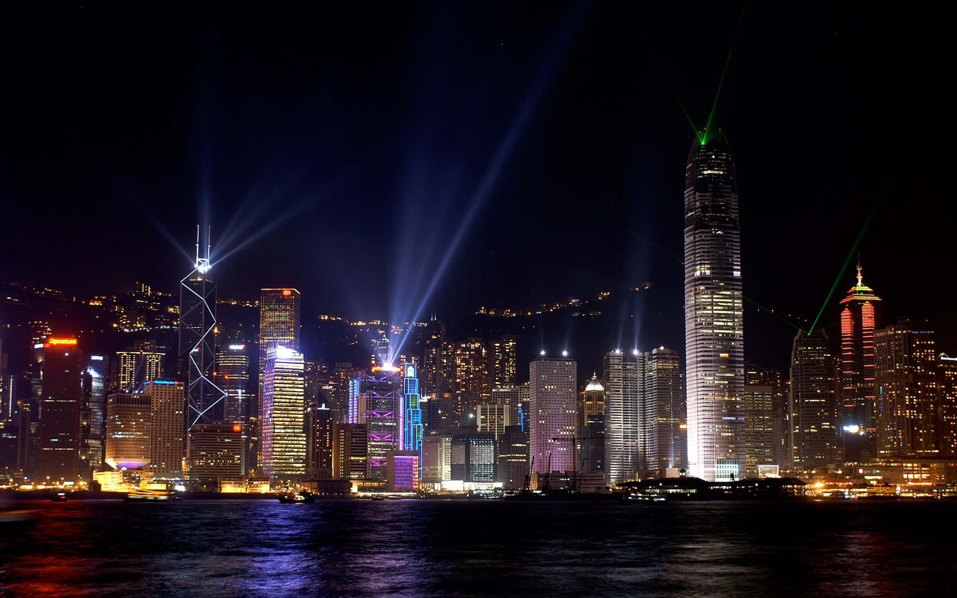 Buildings 桌布 壁紙 — 香港夜景，天際線上有耀眼的雷射光束和色彩繽紛的摩天大樓燈光，倒映在水面上。