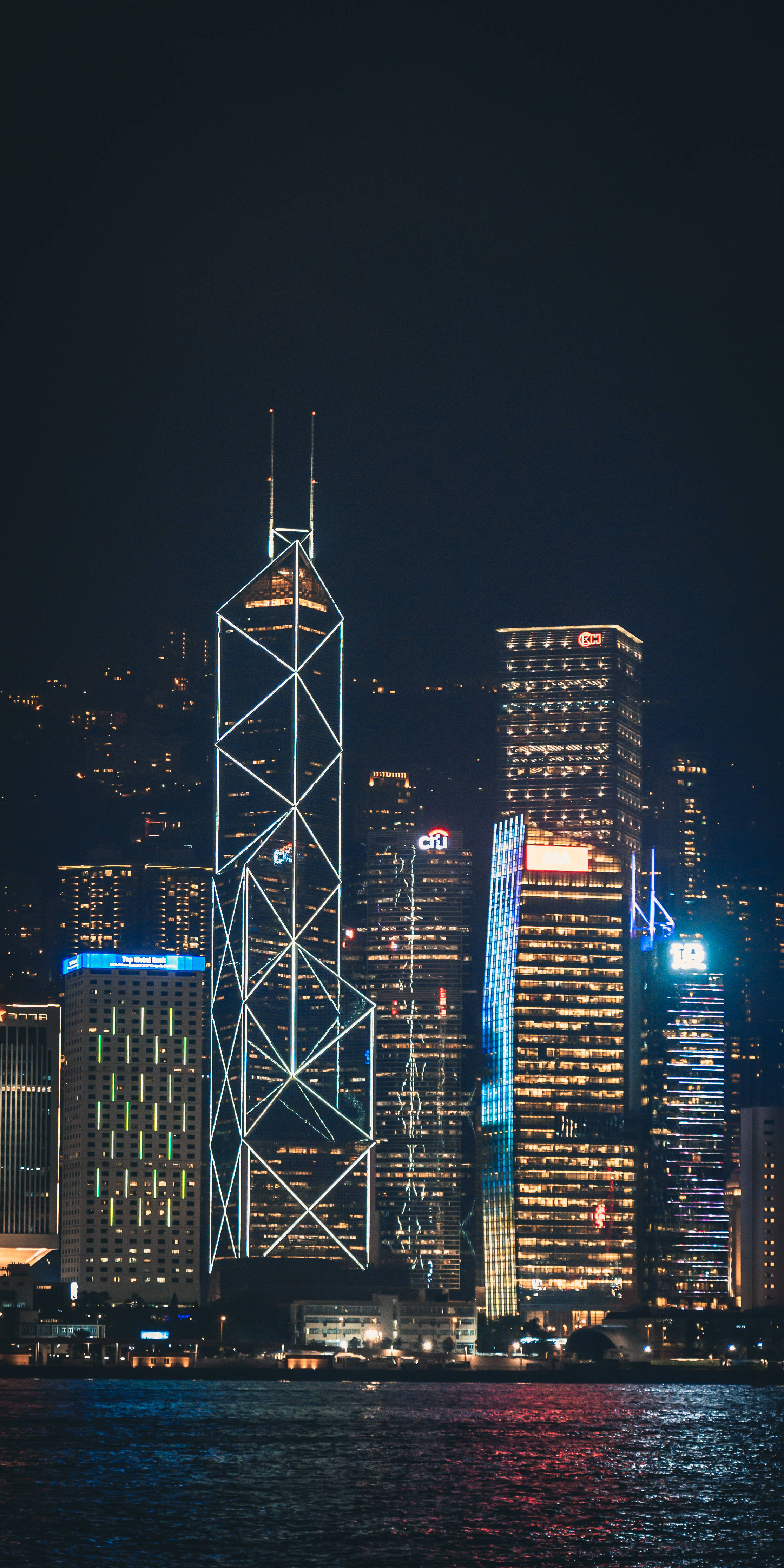 香港 桌布 壁紙 — 香港夜景天際線，在深黑色天空下，明亮的摩天大樓倒映在黑暗的水面上。