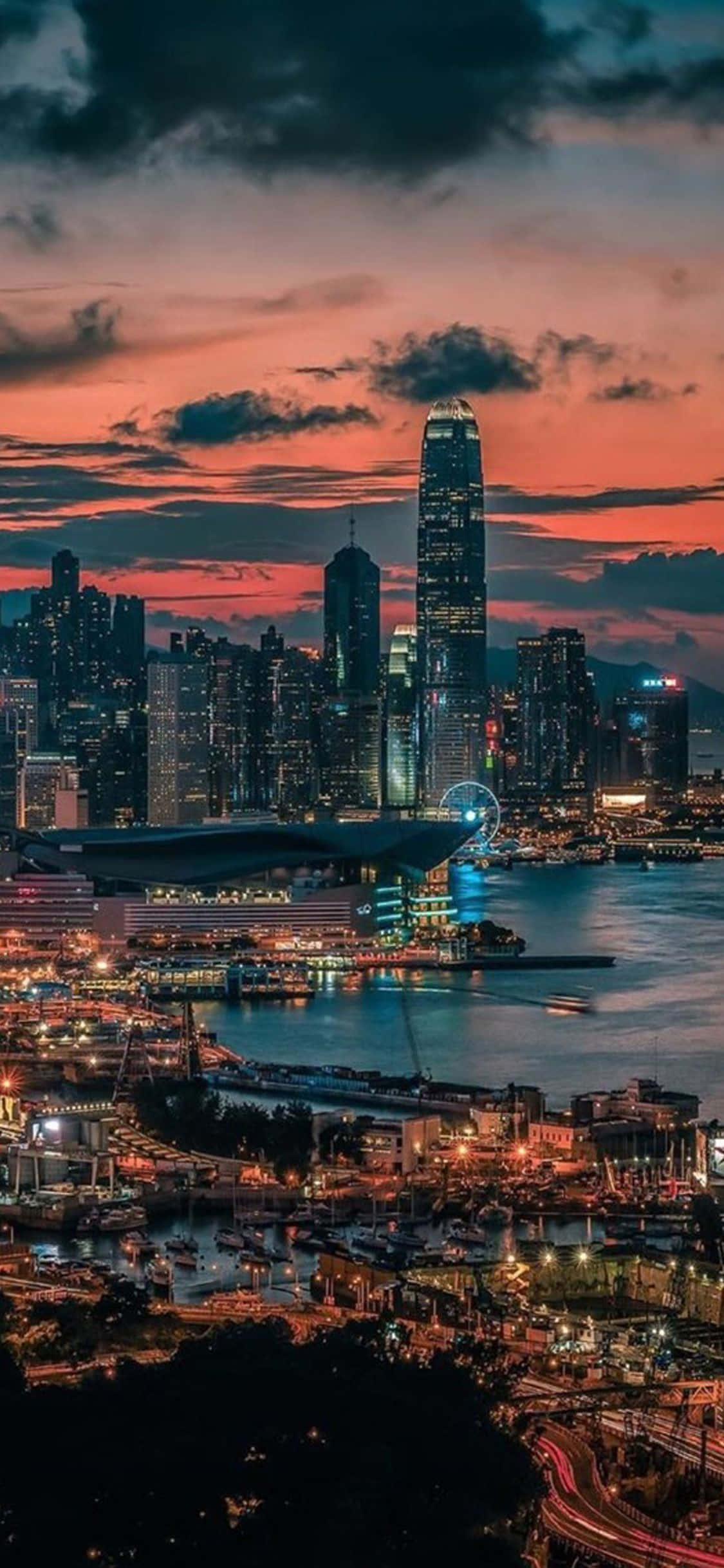 Hong Kong 桌布 壁紙 — 香港天際線上的 vibrant 日落，閃爍的摩天大樓和充滿船隻和燈光的港口。