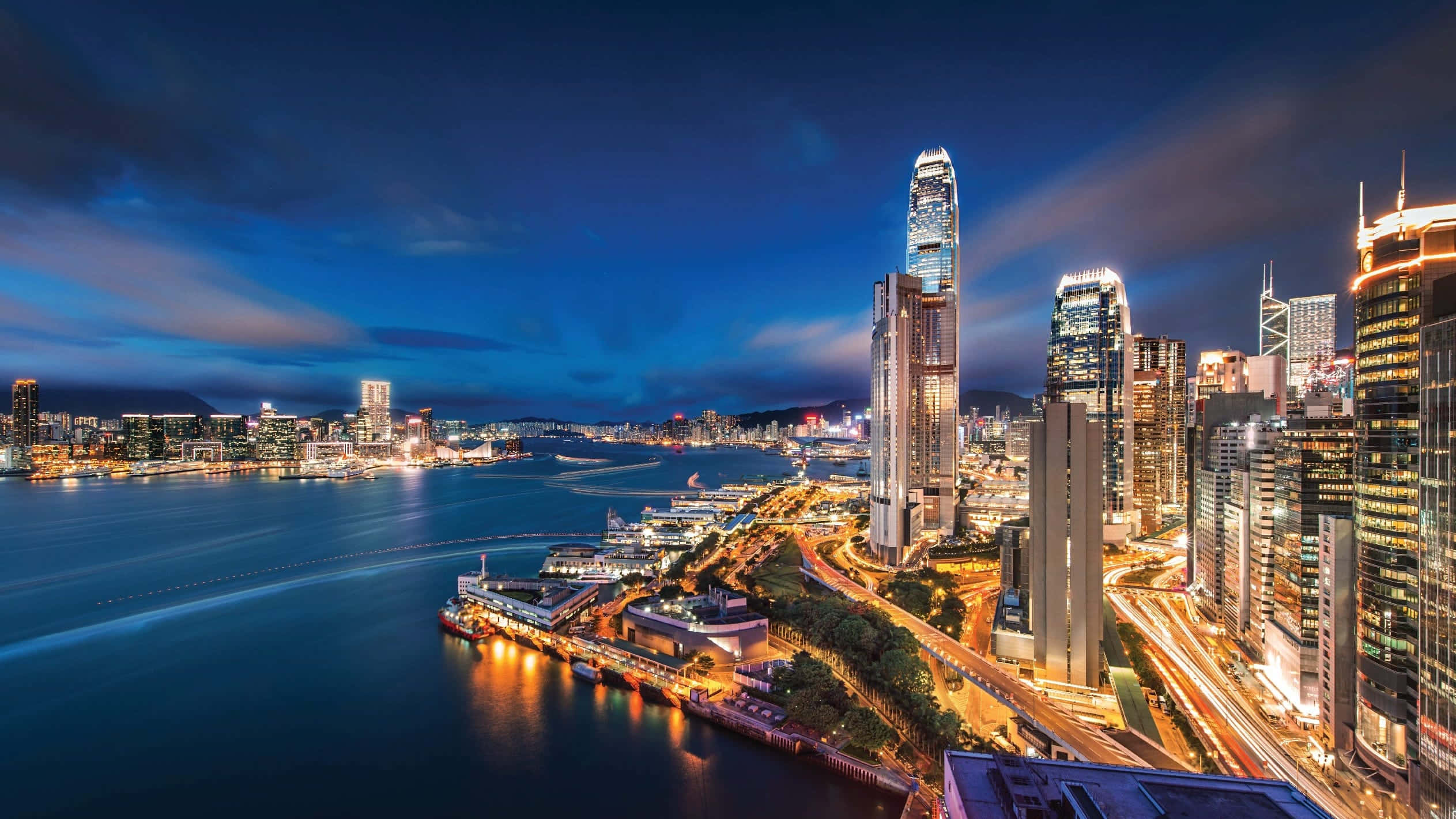 香港 桌布 壁紙 — 香港天際線在暮色中的耀眼景色，發光的摩天大樓倒映在港口水面上。