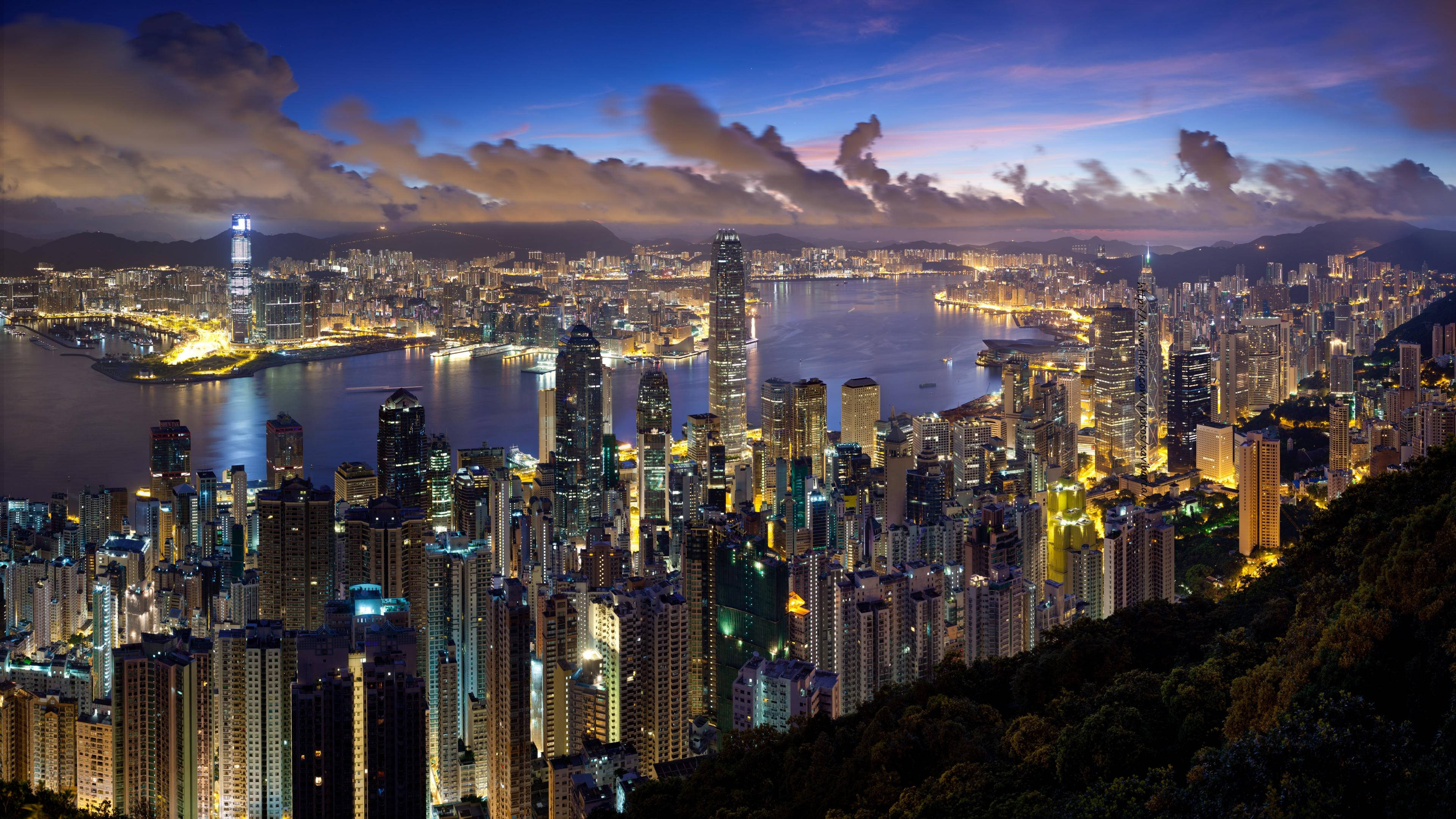 城市 桌布 壁紙 — 香港天際線的壯麗暮色景觀，發光的摩天大樓在戲劇性的紫色和藍色天空下倒映在港灣水面上。