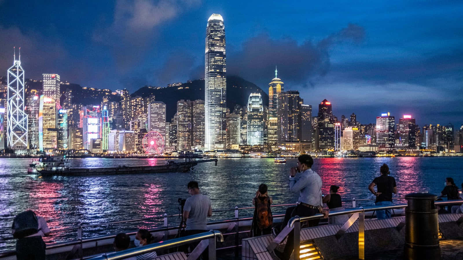 香港 桌布 壁紙 — 香港天際線的活力夜景，閃爍的摩天大樓倒映在水面上，人們在海濱長廊觀賞。