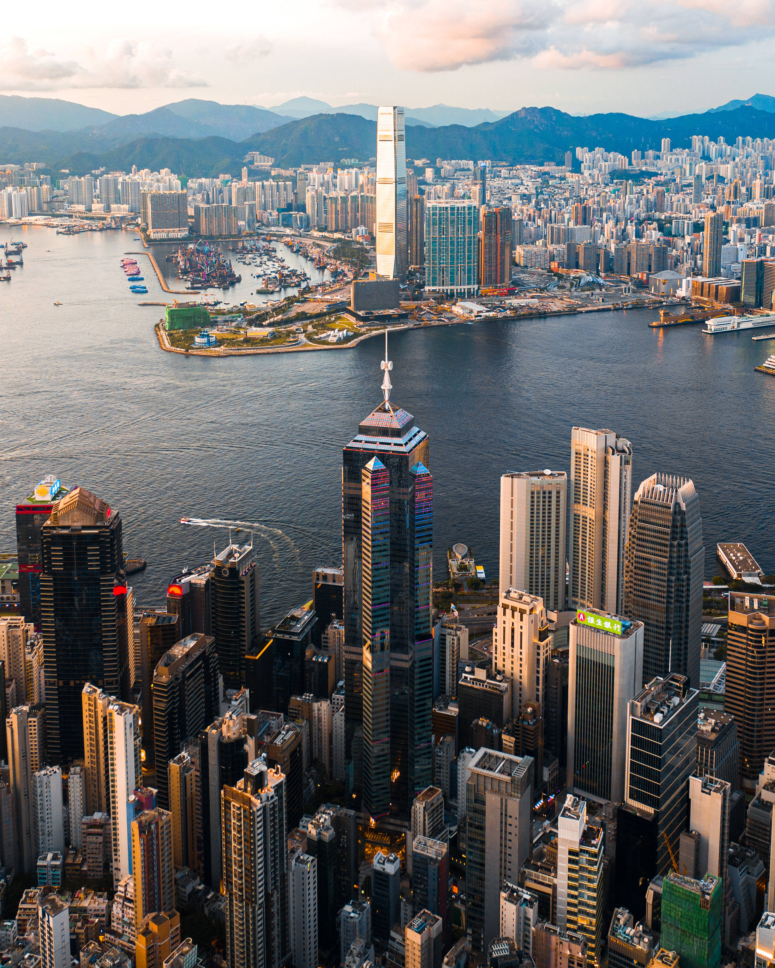 香港 桌布 壁紙 — 香港天際線的鳥瞰圖，日落時分，高聳的摩天大樓在港口和遠處山脈上反射出金色的光芒。