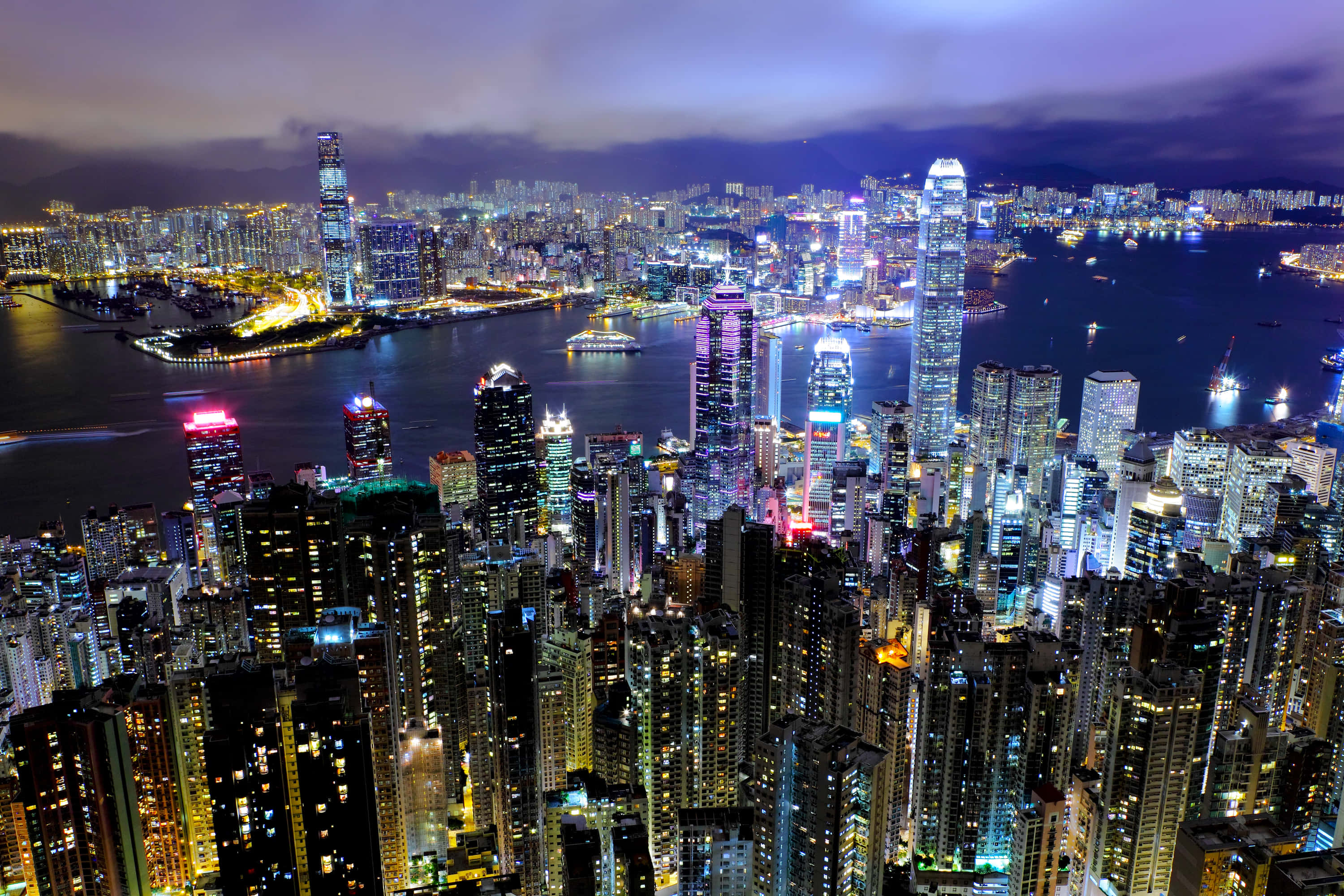 香港 桌布 壁紙 — 香港璀璨天際線的夜間鳥瞰圖，高聳的摩天大樓在港灣水面上反射出霓虹燈光。
