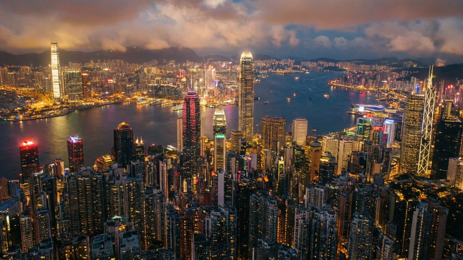 香港黃金時刻 壁紙 — 黃昏時分香港天際線的航拍圖，閃爍的摩天大樓在戲劇性的雲層下倒映在港灣水面上。