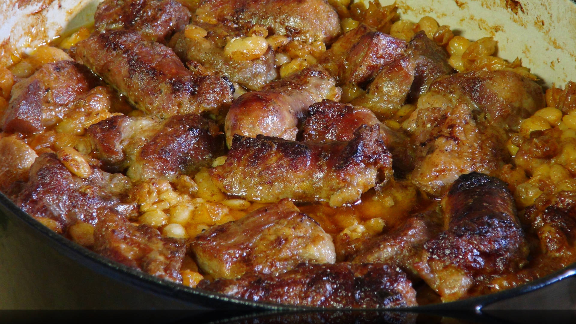 Delicious Food 桌布 壁紙 — 香脆金黃的香腸塊在濃郁的金色醬汁中與白豆一起在鑄鐵鍋中滋滋作響。