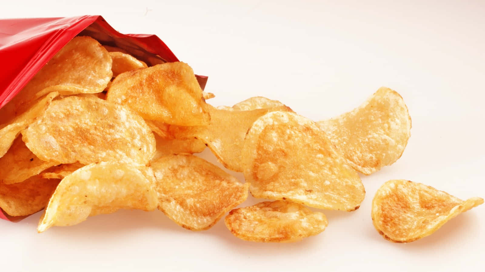 Snacks 桌布 壁紙 — 香脆金黃色薯片從紅色包裝袋中灑出，背景為潔白乾淨。