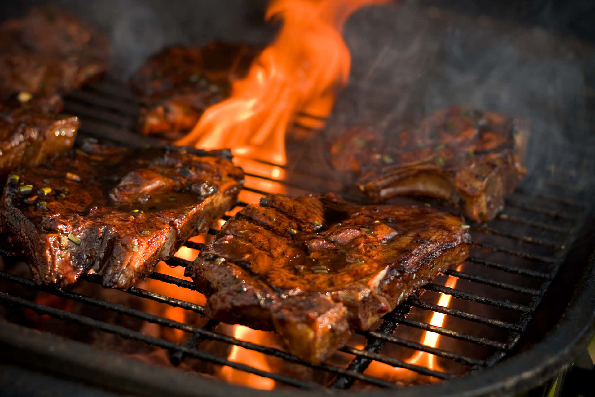 meat 桌布 壁紙 — 香草調味的烤肋骨在明亮的橙色火焰上滋滋作響，烤架上煙霧升騰。