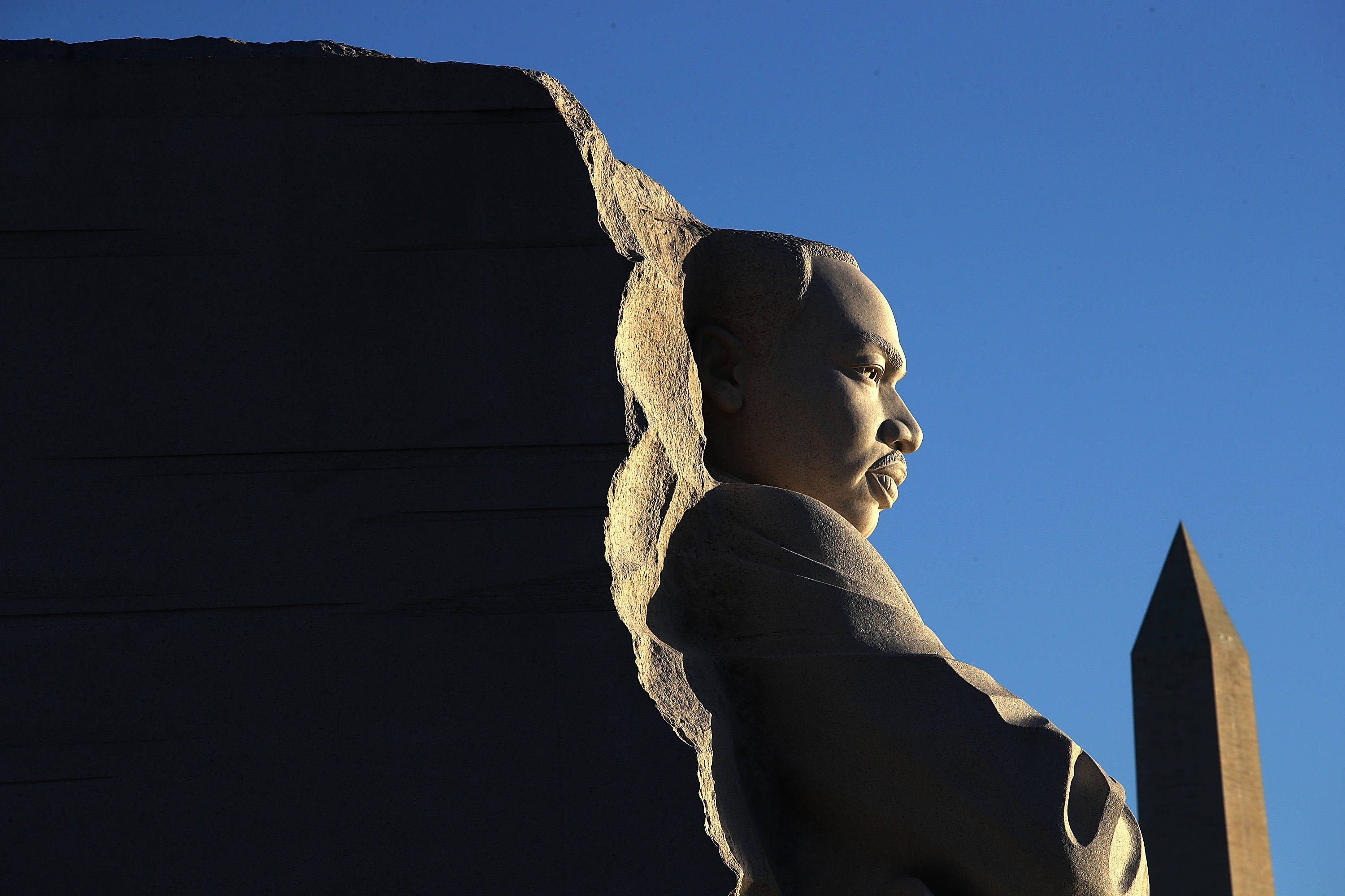 馬丁·路德·金恩 動圖 桌布 壁紙 — 馬丁·路德·金恩的強力石像側面，襯著晴朗藍天，遠處是華盛頓紀念碑。