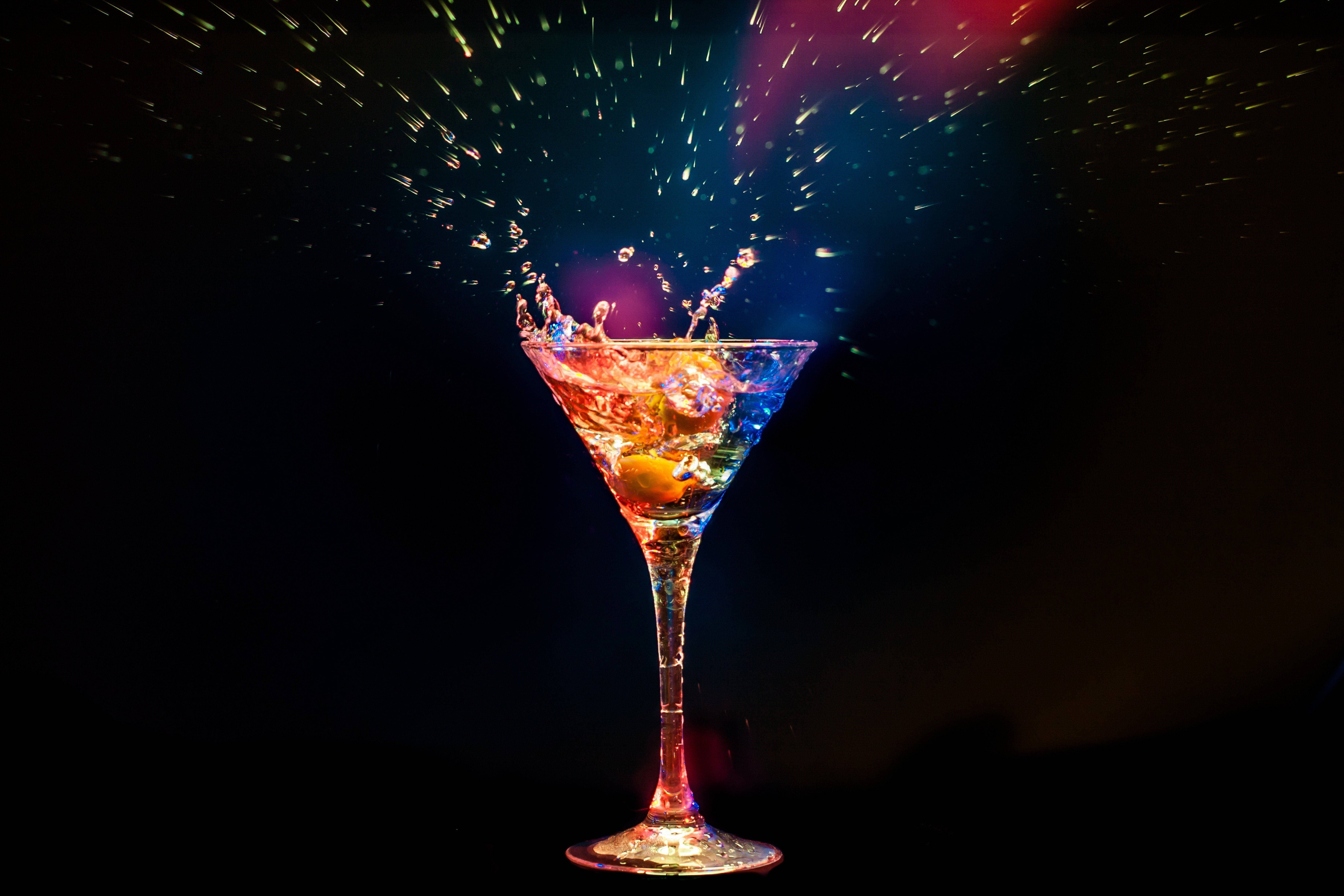Drink 桌布 壁紙 — 馬丁尼杯在黑暗背景下噴出色彩繽紛的液體和閃爍的火花。