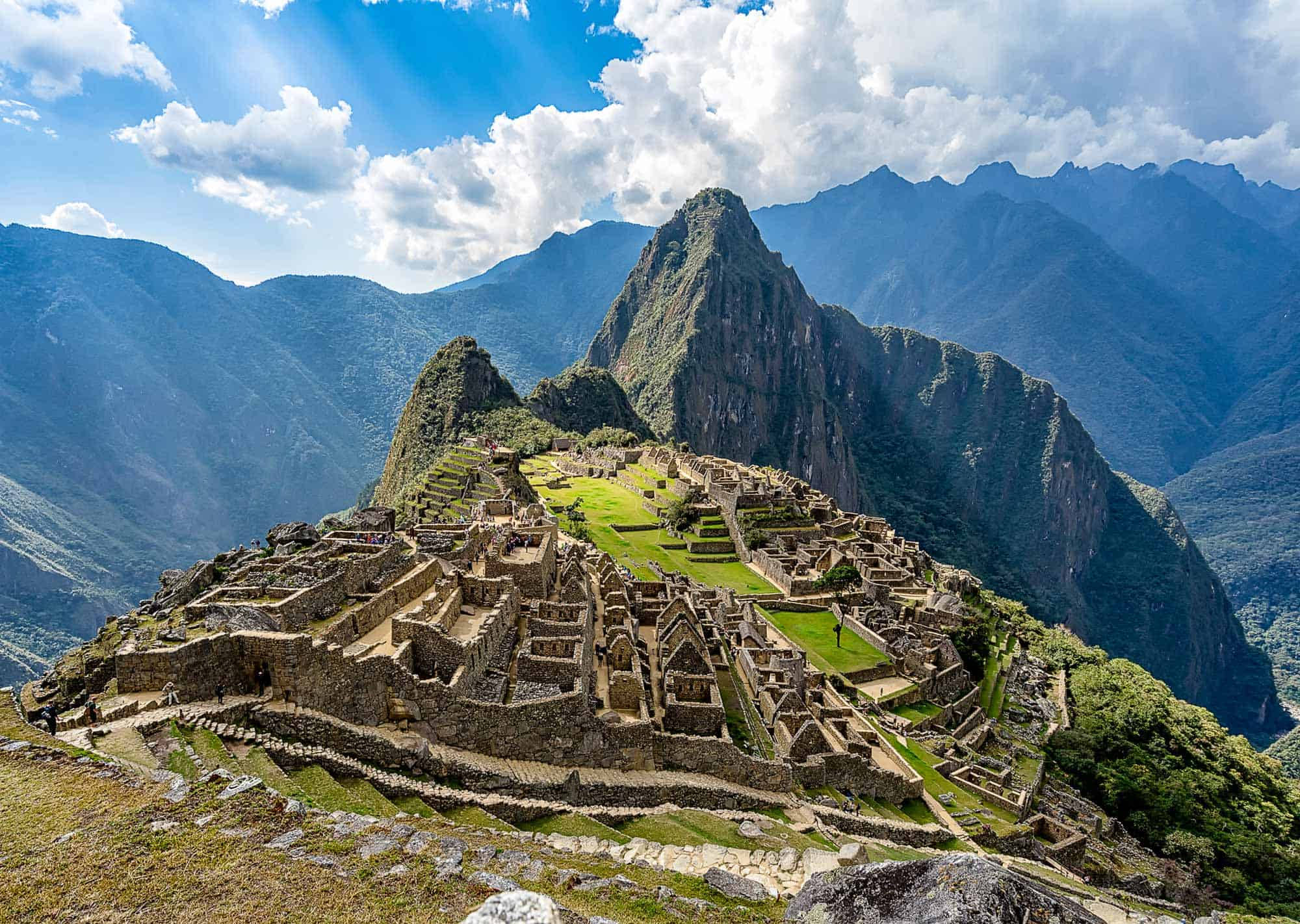 山景 桌布 壁紙 — 馬丘比丘的古老石遺跡在陽光普照的山脊上延伸，天空湛藍，白雲朵朵。